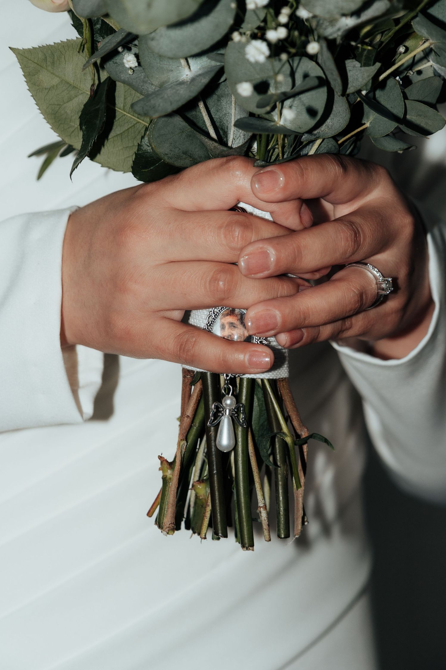 Close-up of bride's hands with silver rings holding green stem bouquet of roses and eucalyptus.