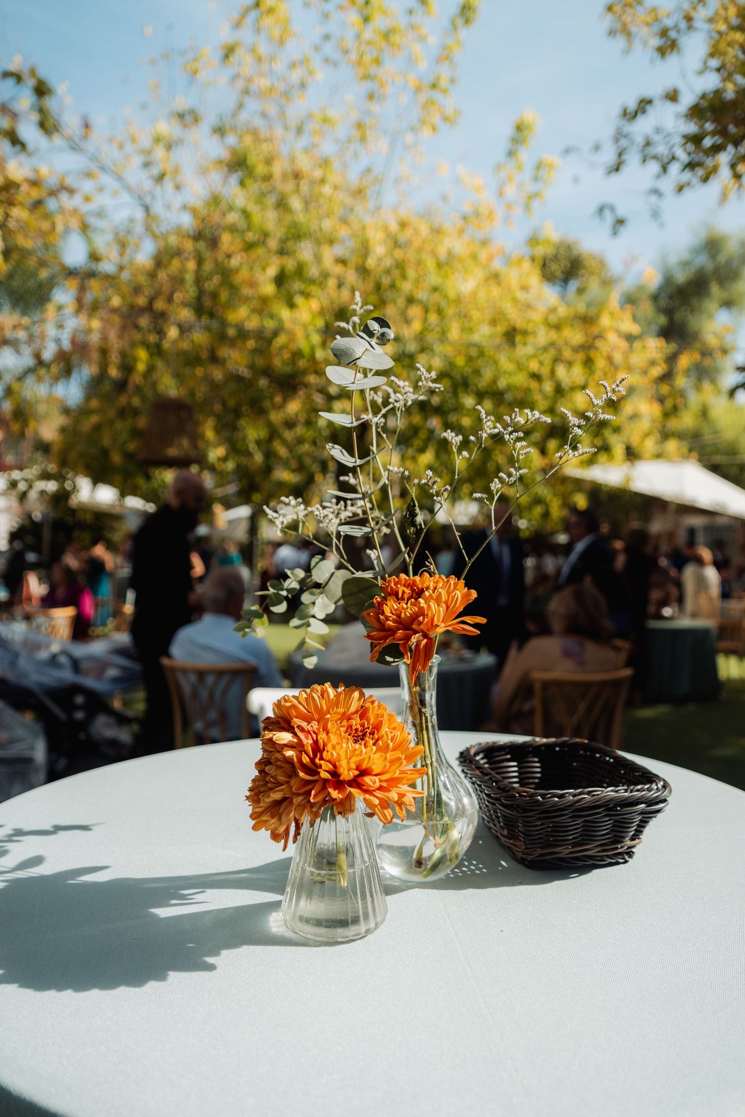 Orange chrysanthemum flowers in glass vases on white outdoor wedding table.