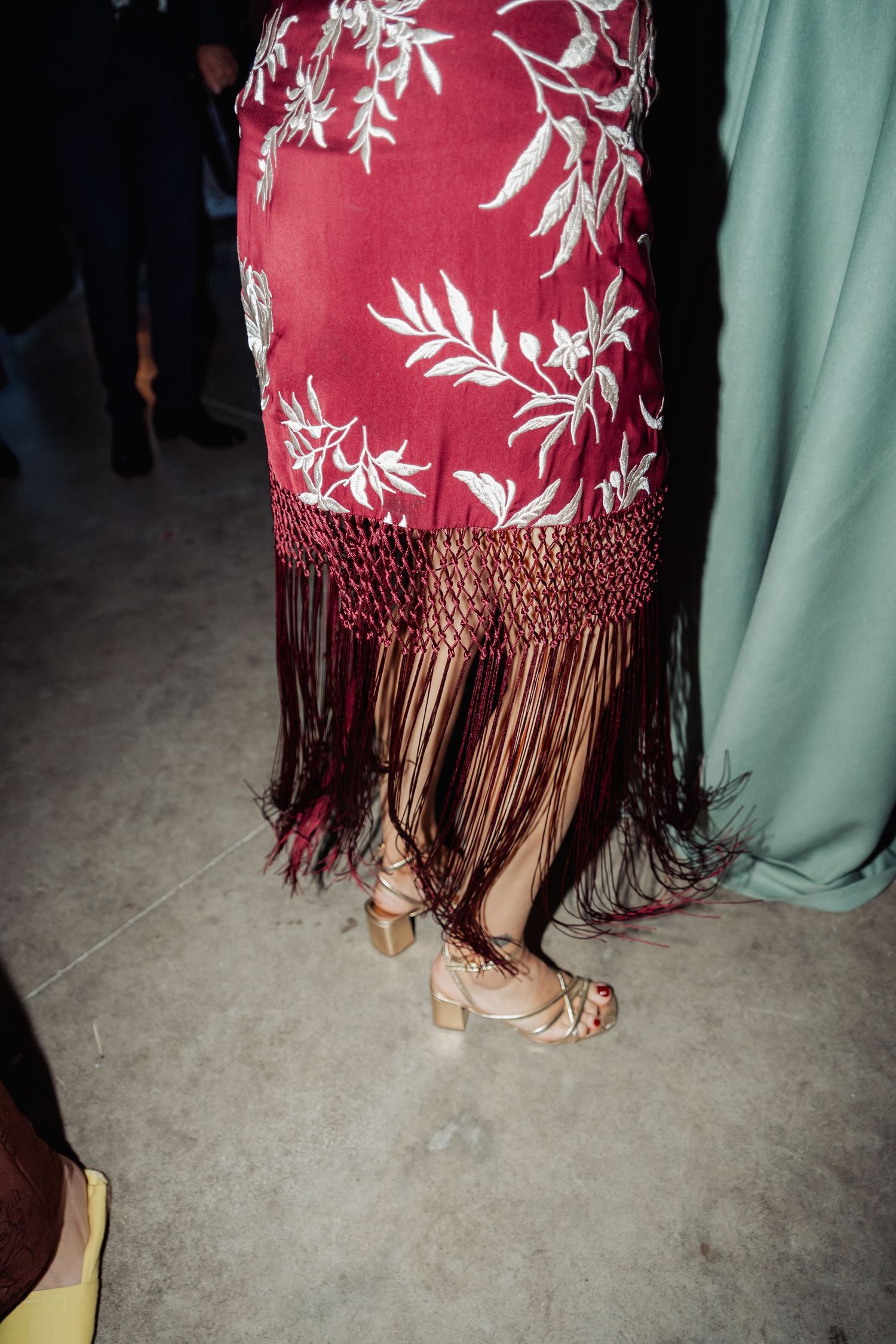 Close-up of a red floral dress with fringe hem and beige block heels on a dance floor.