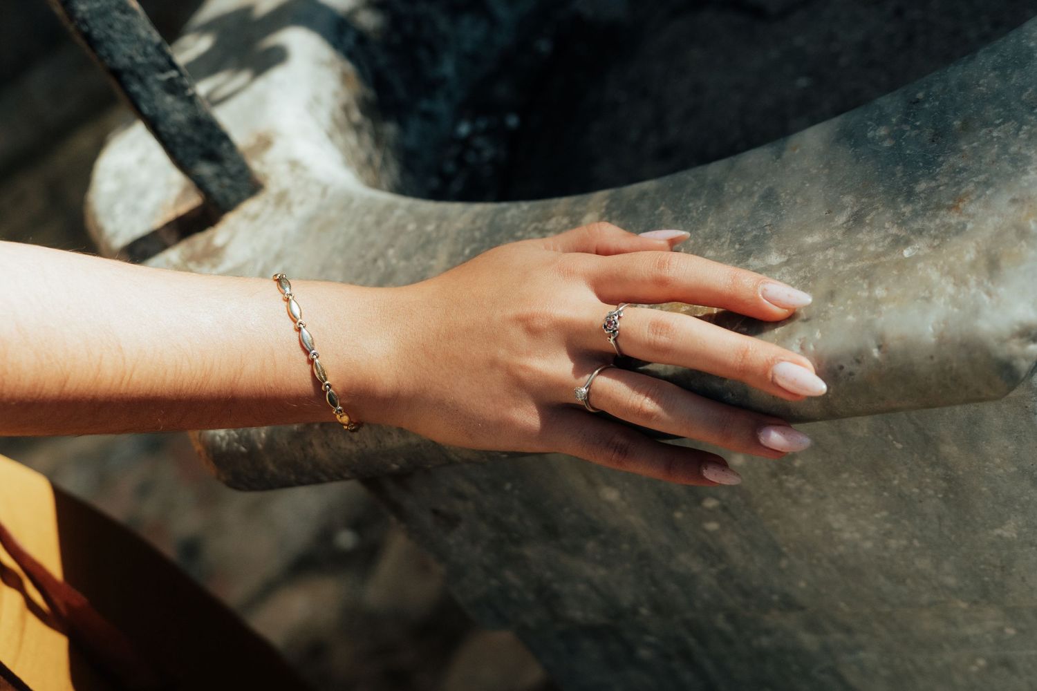 A woman's hand adorned with a delicate gold bracelet and rings rests gracefully on a stone surface.