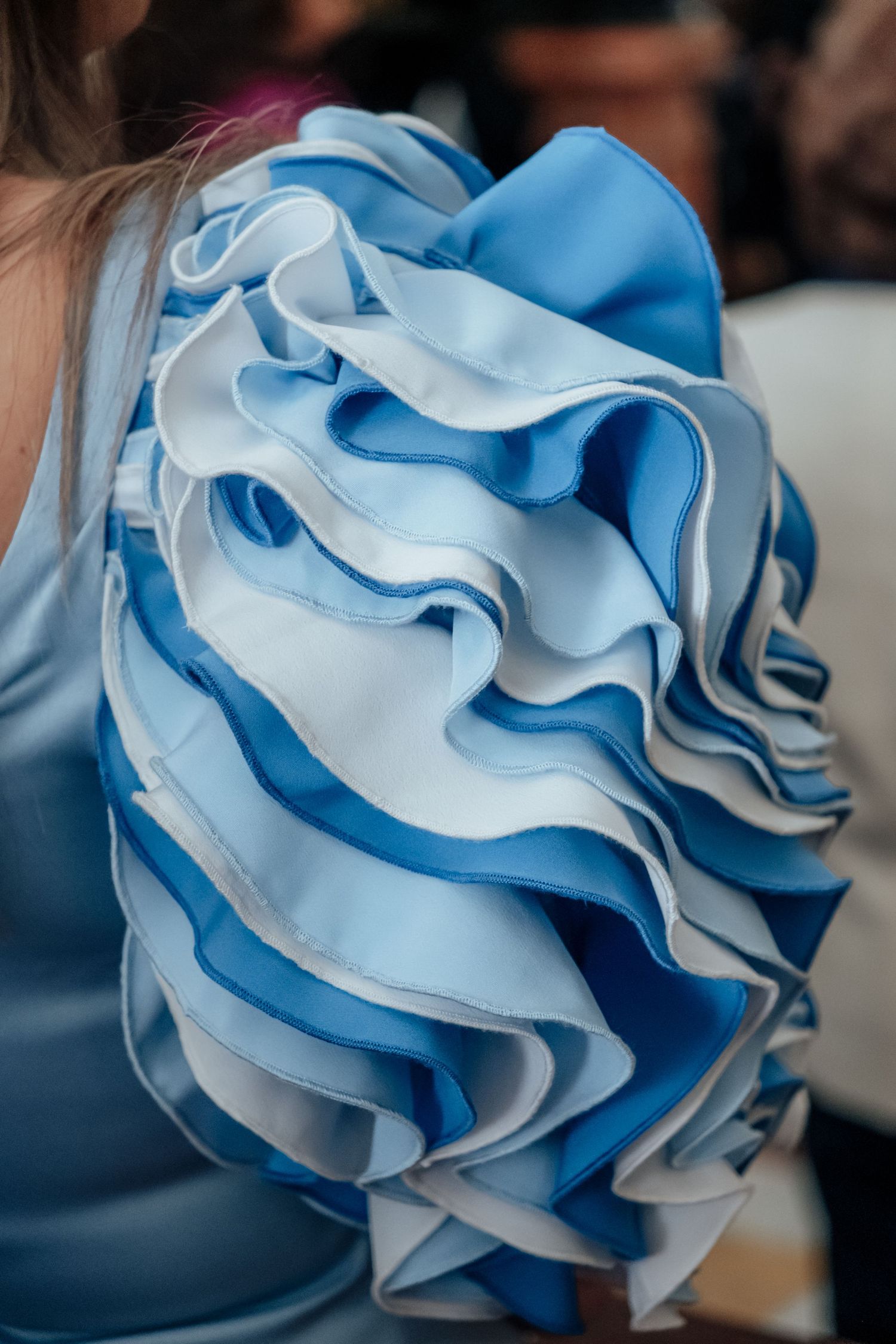 Close-up detail of layered blue and white ruffled sleeve on elegant formal dress at wedding event.