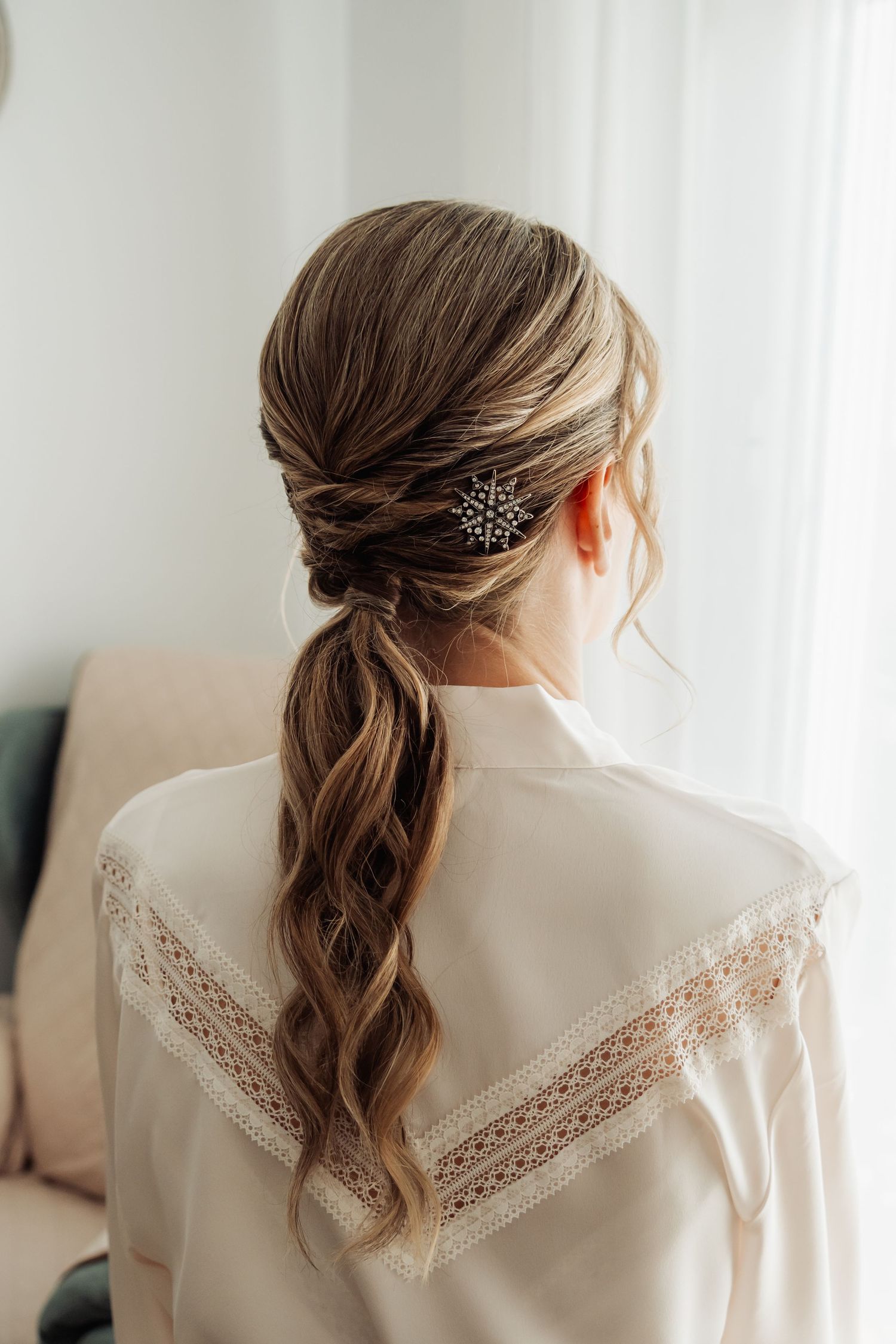 Bride with elegant braided ponytail hairstyle adorned with snowflake hair pin, rear view.