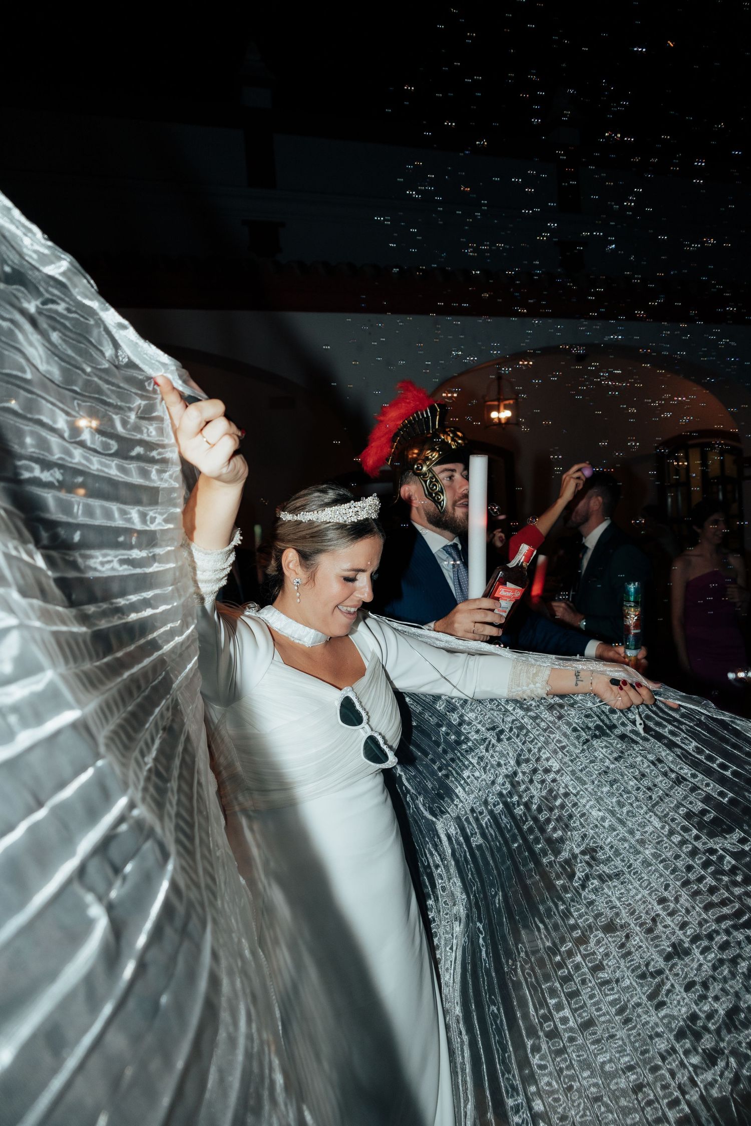 Bride in white dress dancing with silver wings under confetti at a wedding reception.