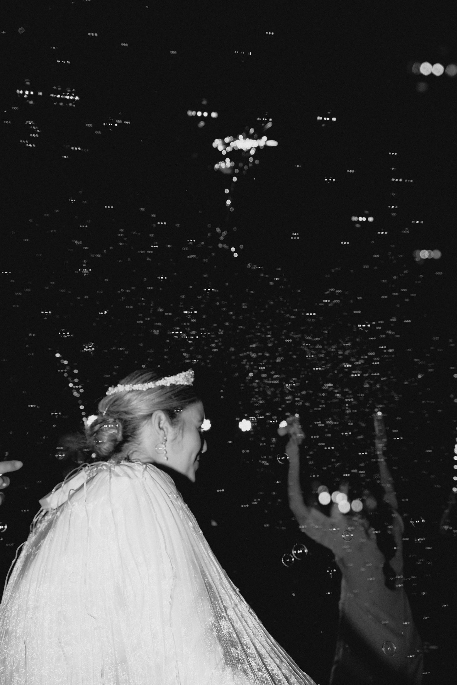 Black and white photo of a bride surrounded by confetti and bubbles at a nighttime wedding celebration.