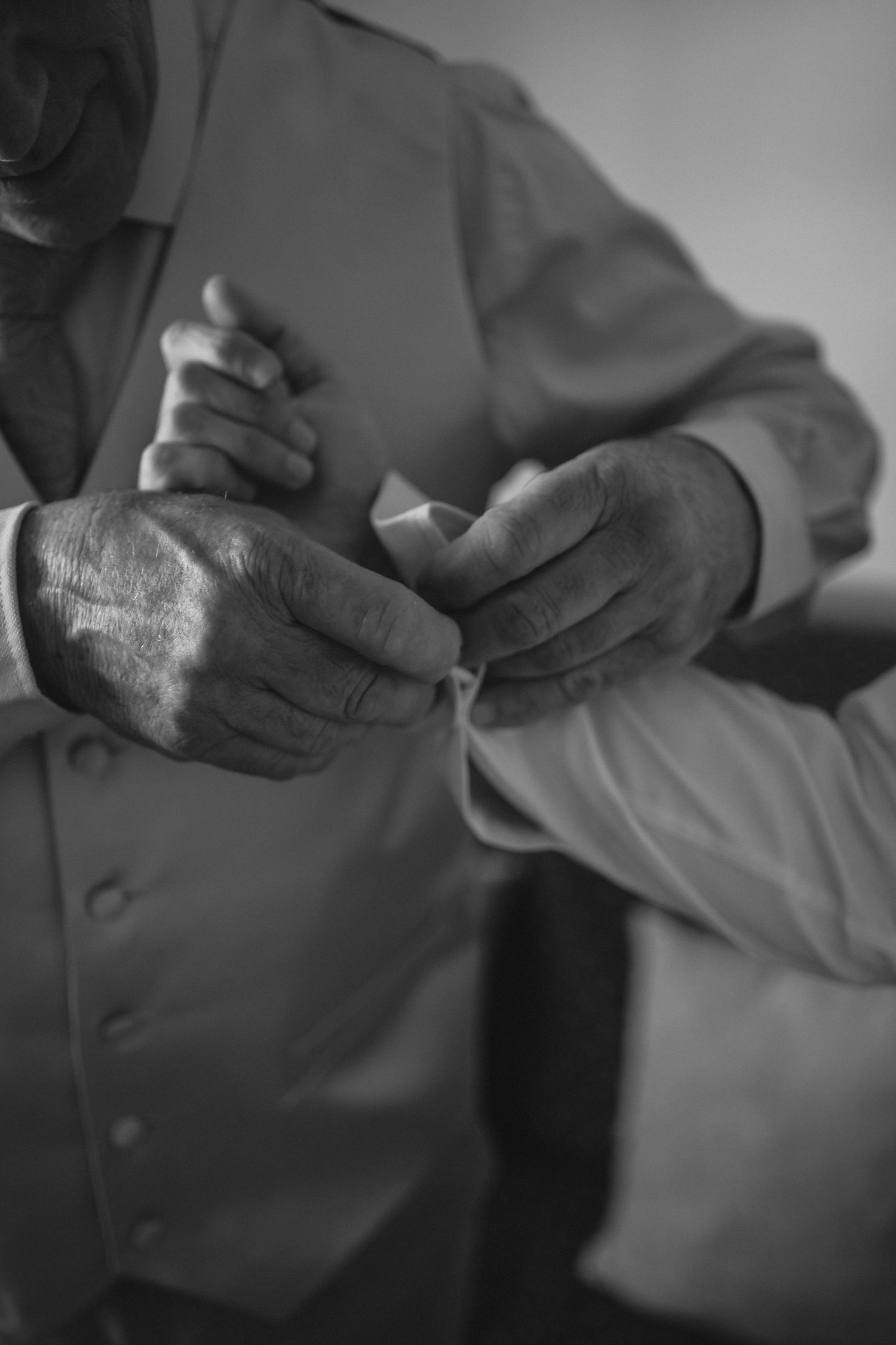 Close-up black and white photo of hands helping button a dress shirt sleeve.