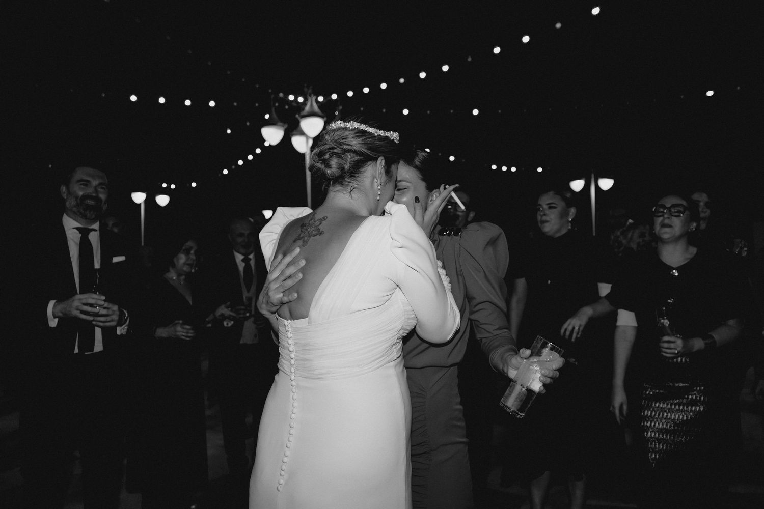 Black and white photo of bride sharing kiss with guest at outdoor wedding reception.