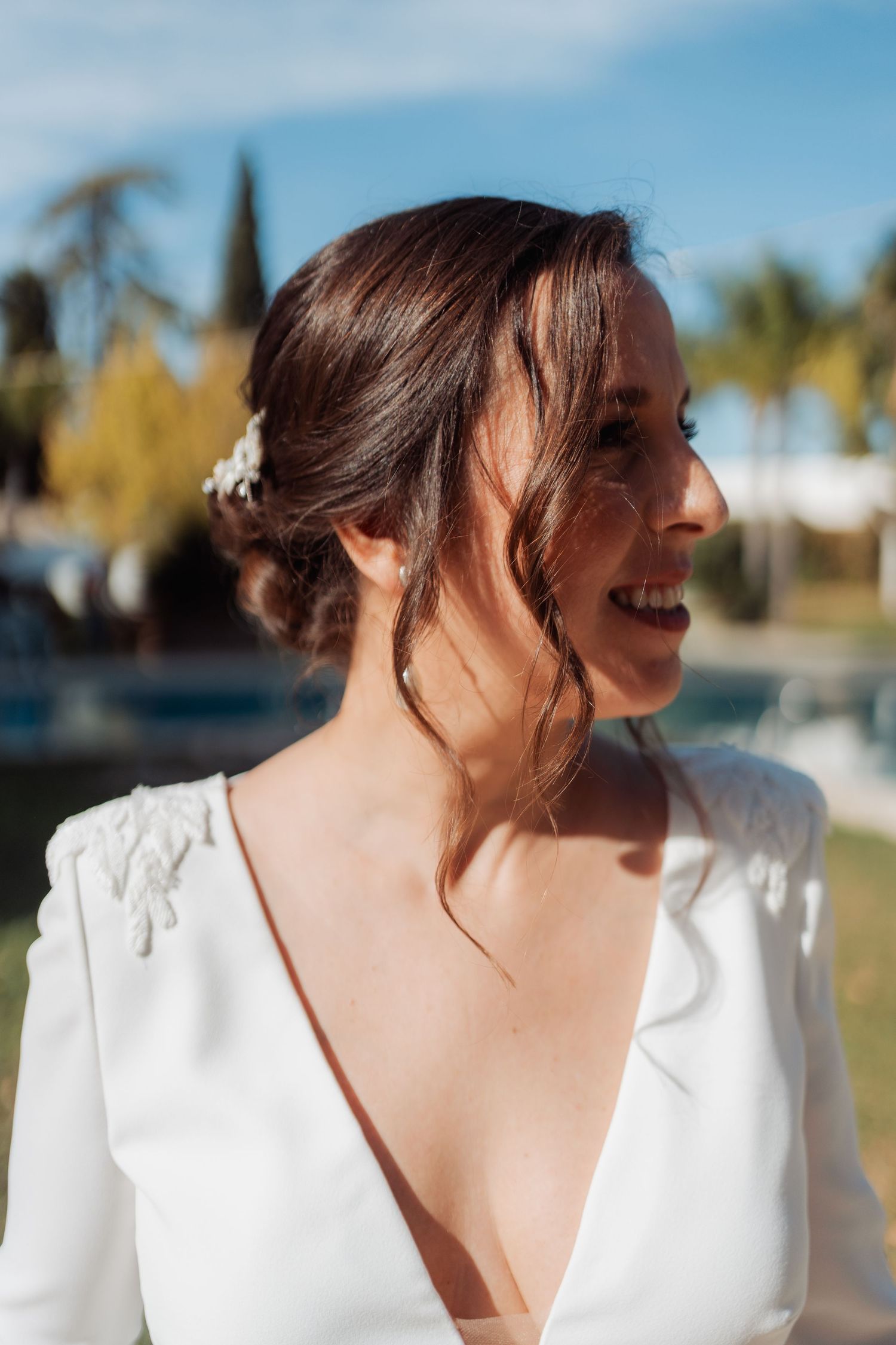Smiling bride in low-back white dress with elegant updo and floral hair accessory.