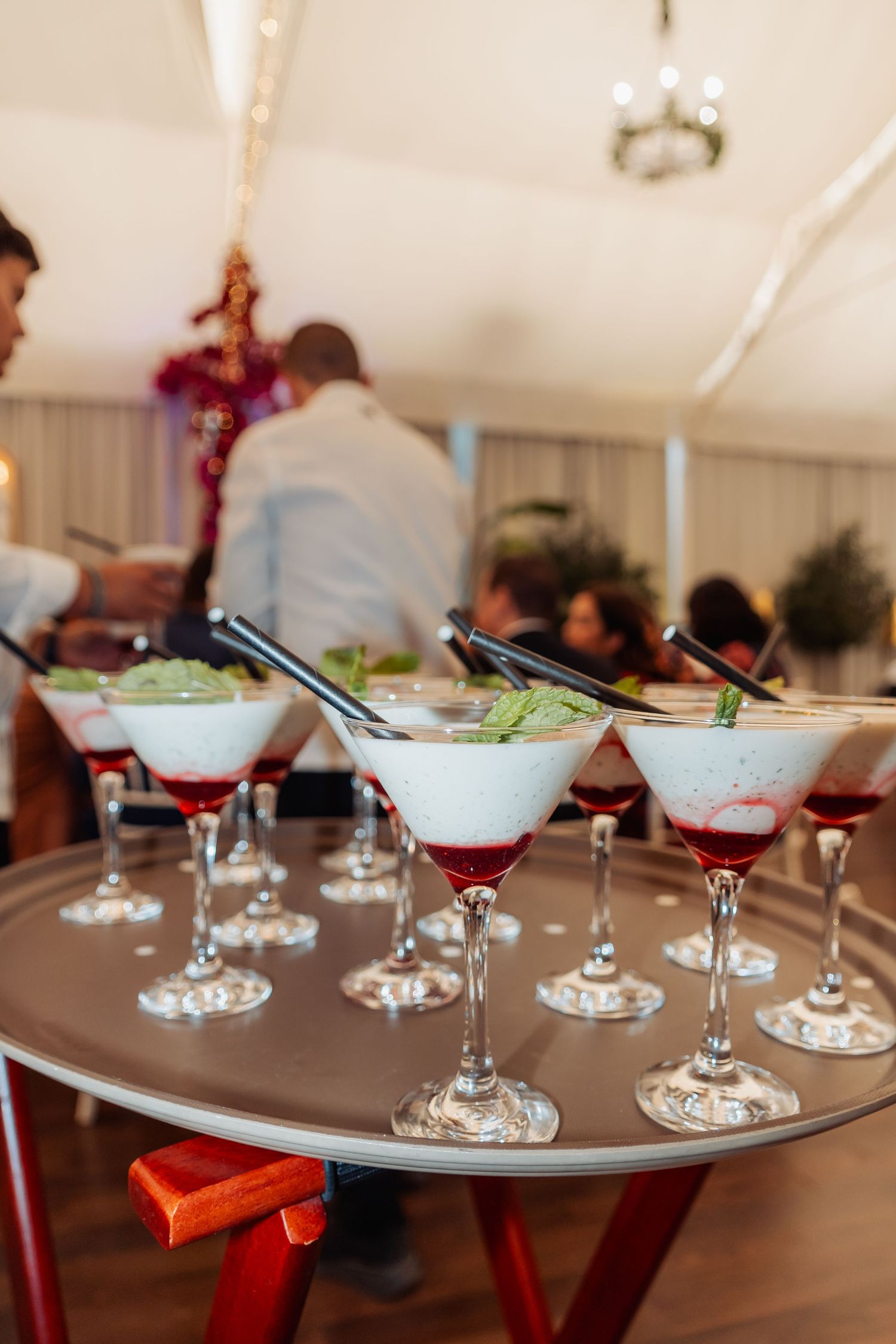 Elegant martini glasses with creamy cocktails and red berry garnish arranged on a round tray at a wedding reception.