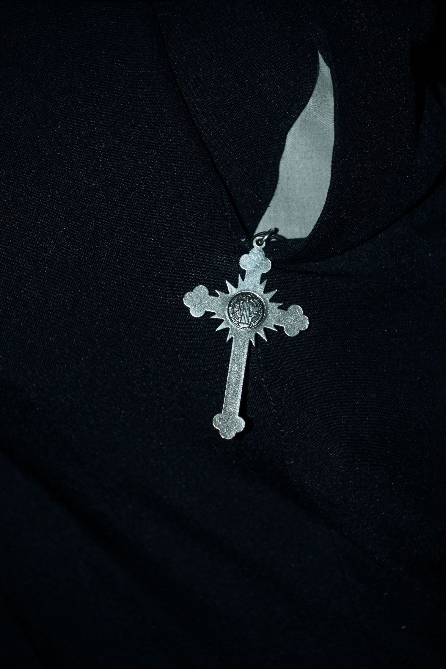 Silver ornate cross pendant necklace displayed against a dark black fabric background.