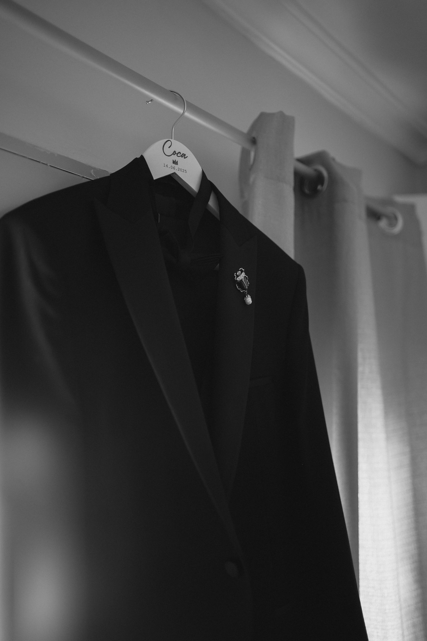 Black tuxedo jacket with lapel pin hanging on custom branded hanger in black and white.