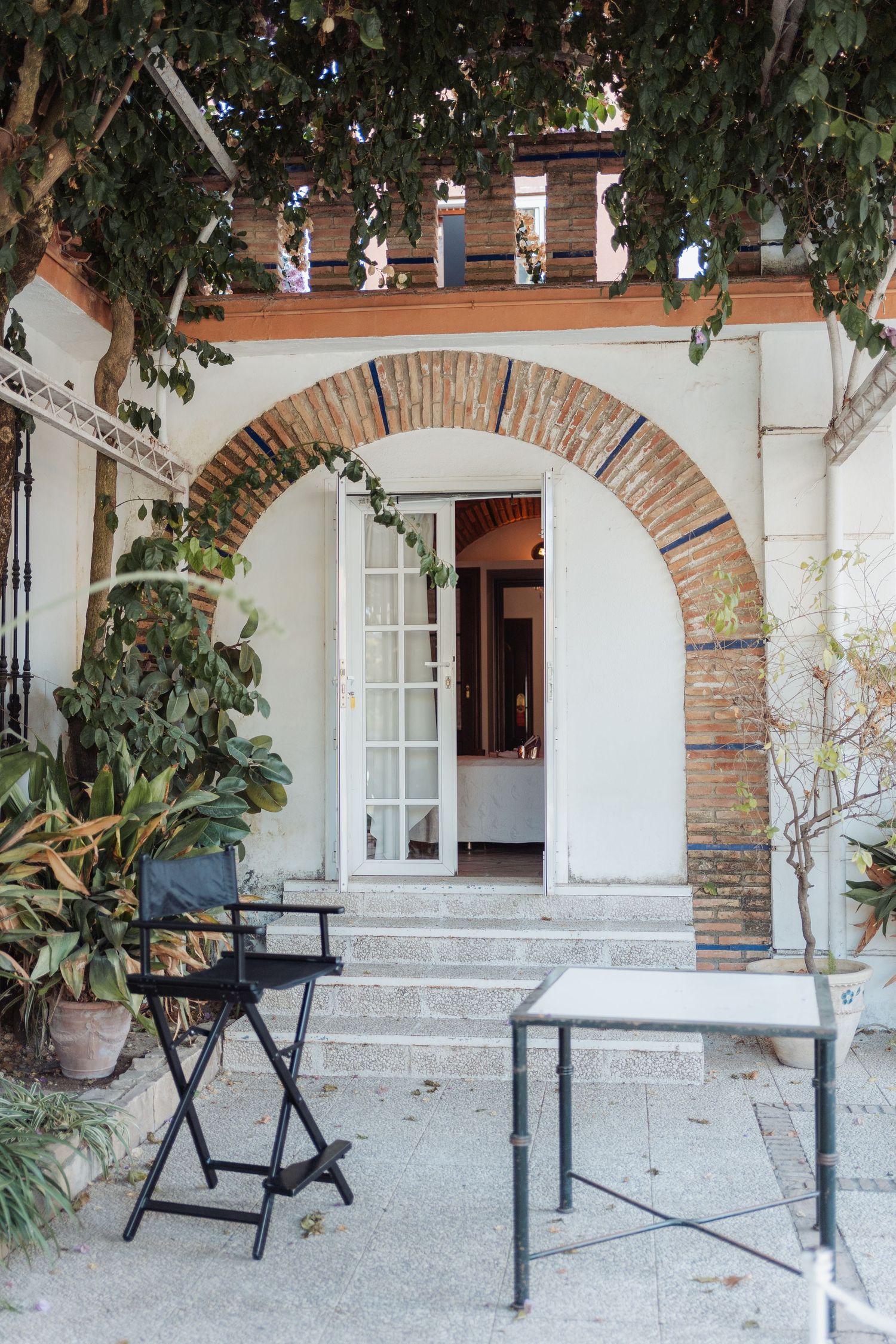 Elegant villa entrance with brick archway, director chair, and lush garden greenery.