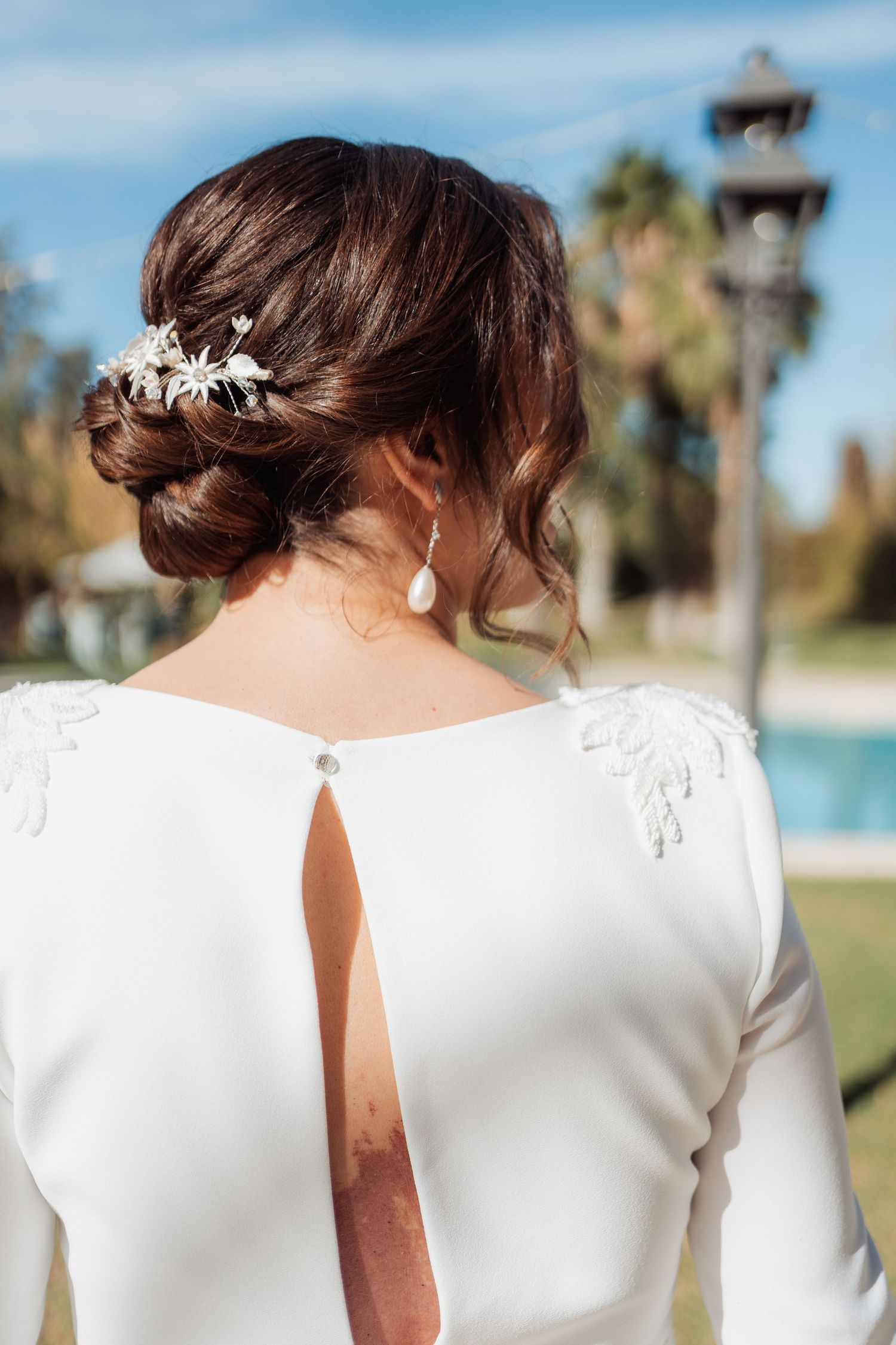 Bride's elegant updo with floral hairpiece and open-back white wedding dress detail outdoors.