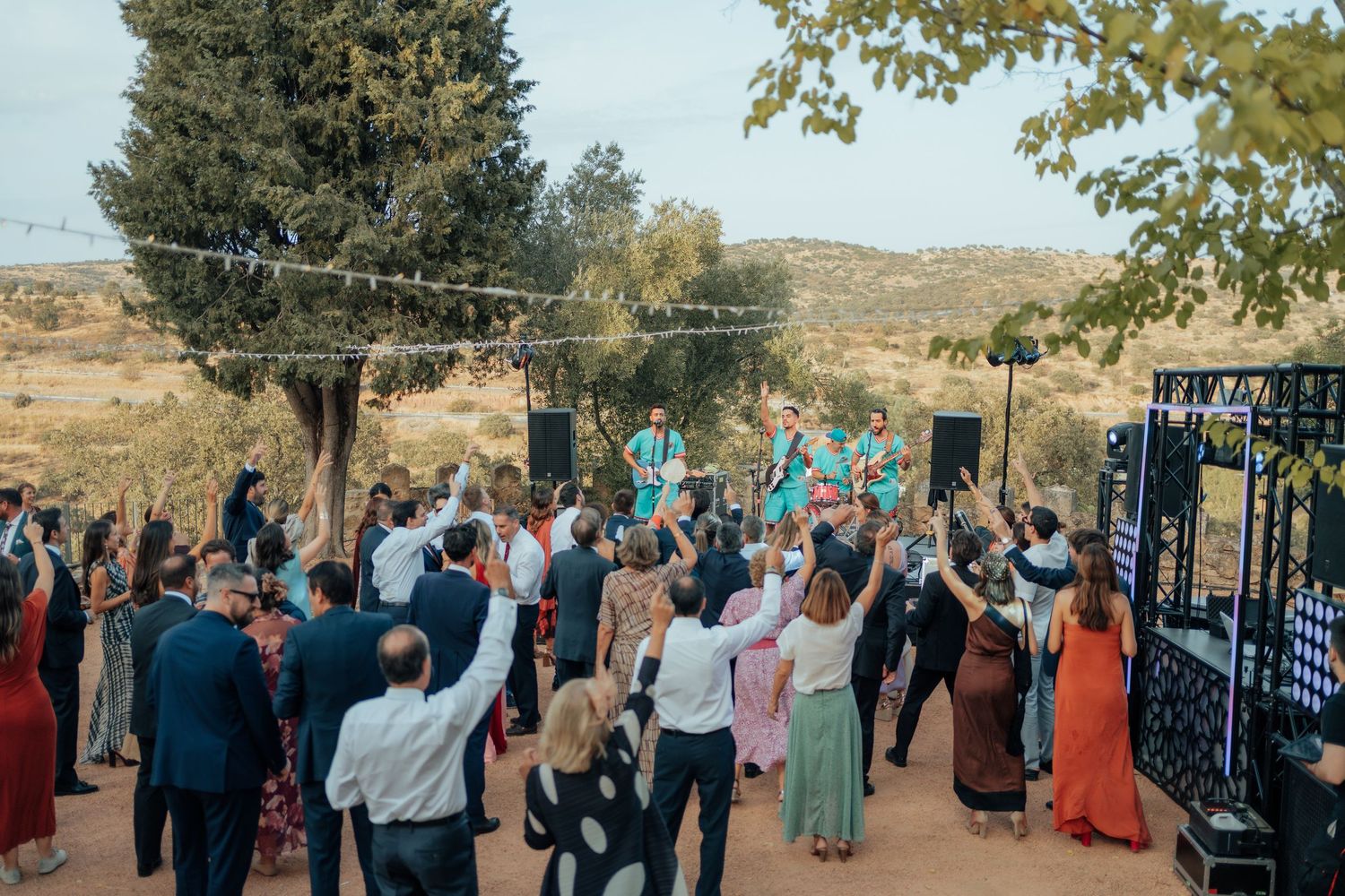 Wedding guests dancing outdoors under string lights with scenic landscape in the background.