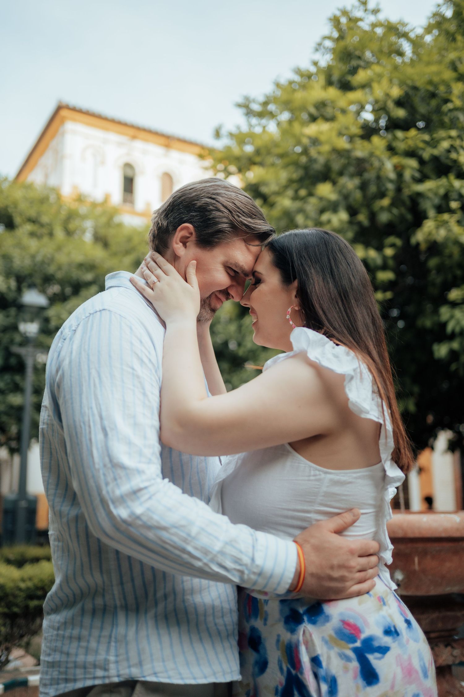 Romantic couple embracing and touching foreheads in a lush outdoor garden setting.