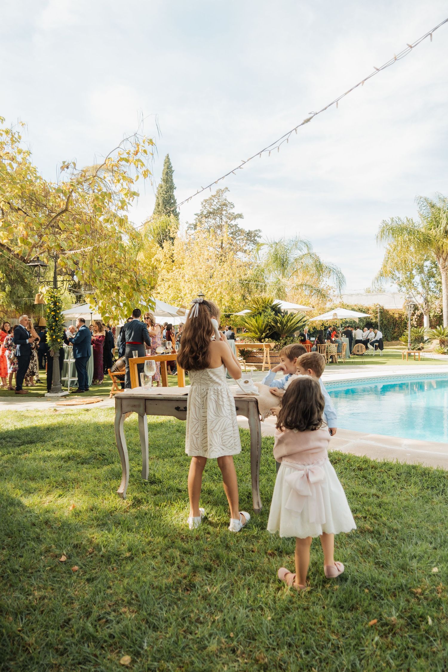 Children and woman at outdoor wedding table beside a swimming pool.