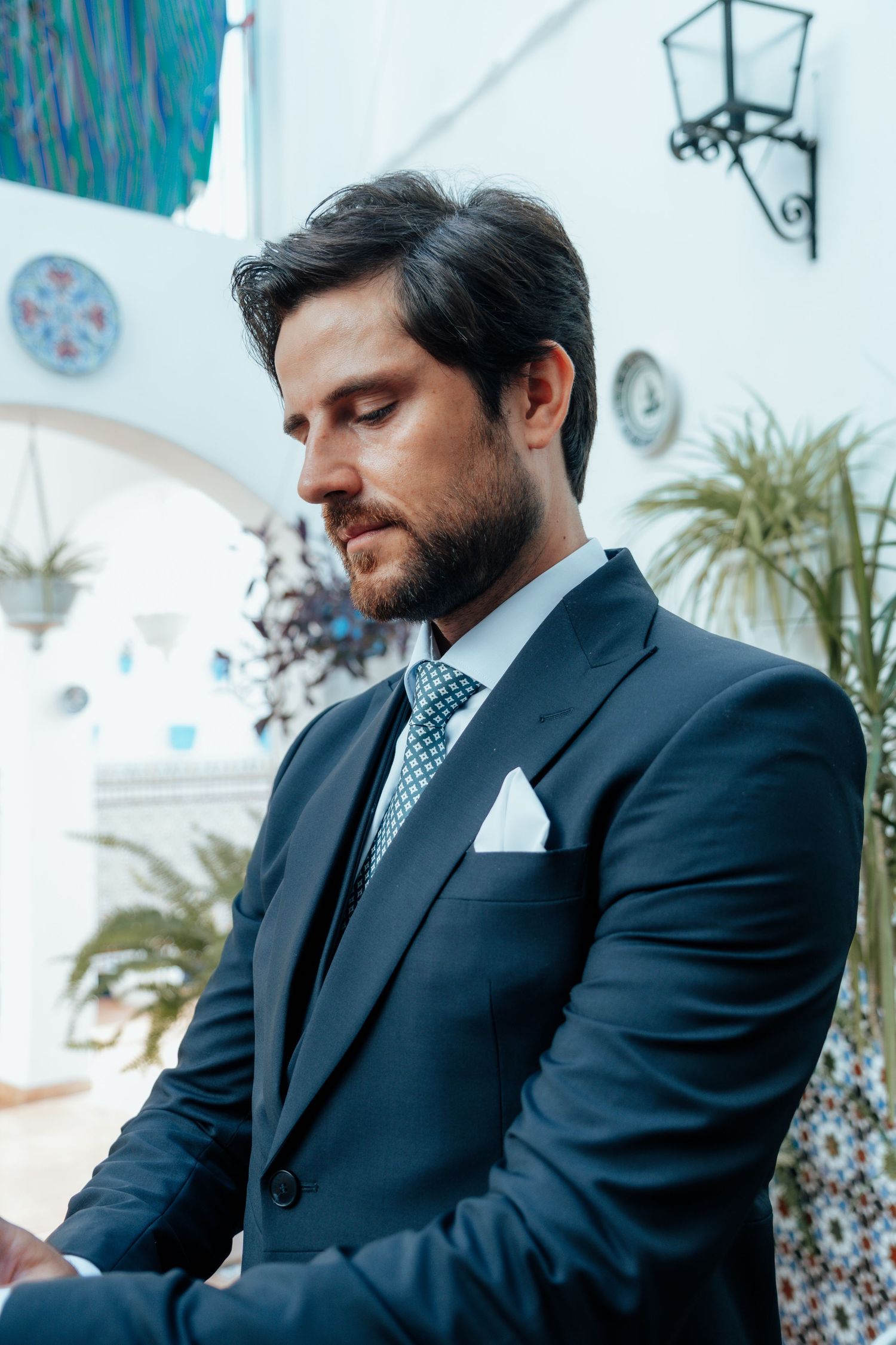 Handsome bearded groom in navy suit with blue tie and white pocket square at Spanish wedding venue.