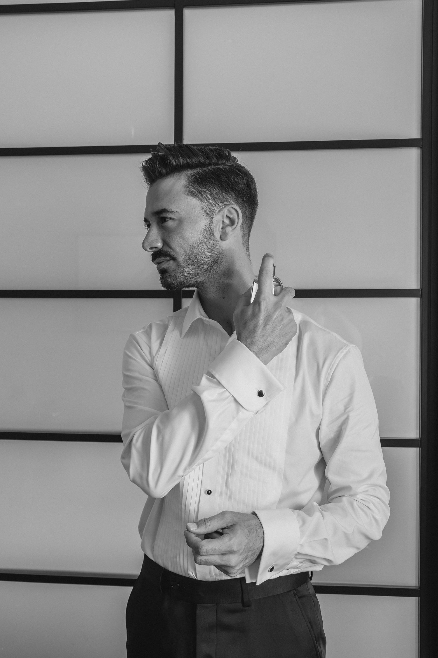 Elegant groom in a white dress shirt adjusting his cufflinks in a black and white portrait.