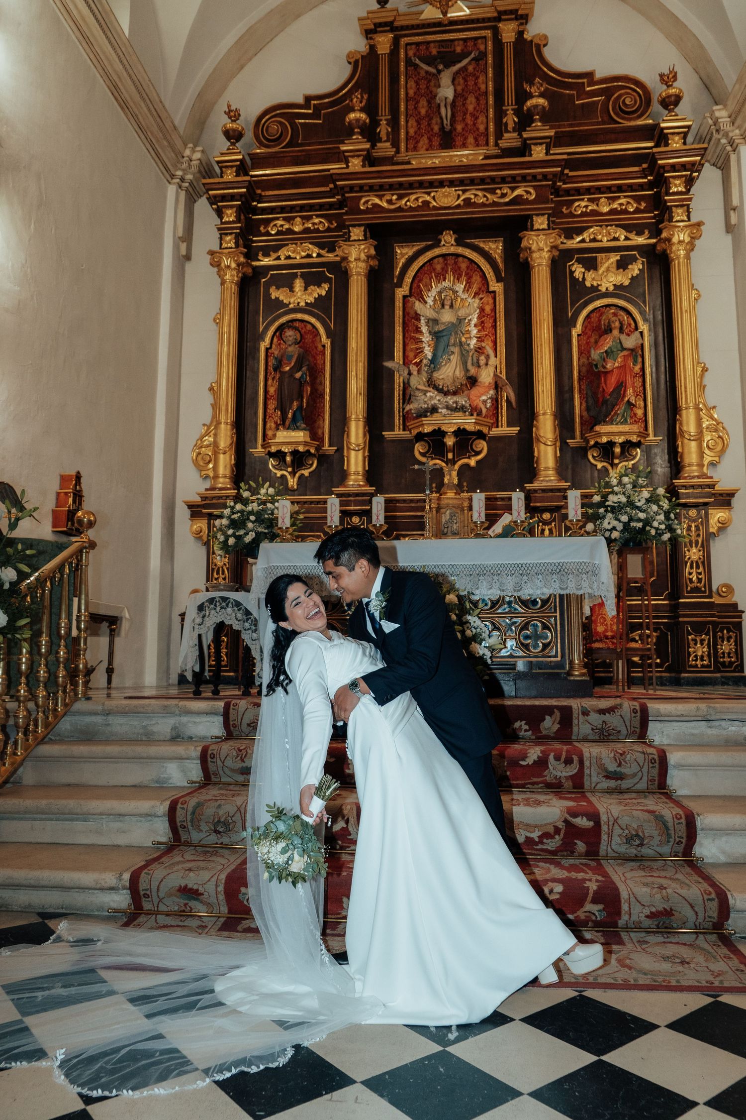 Bride and groom share romantic dip pose before ornate golden baroque altar in historic church.
