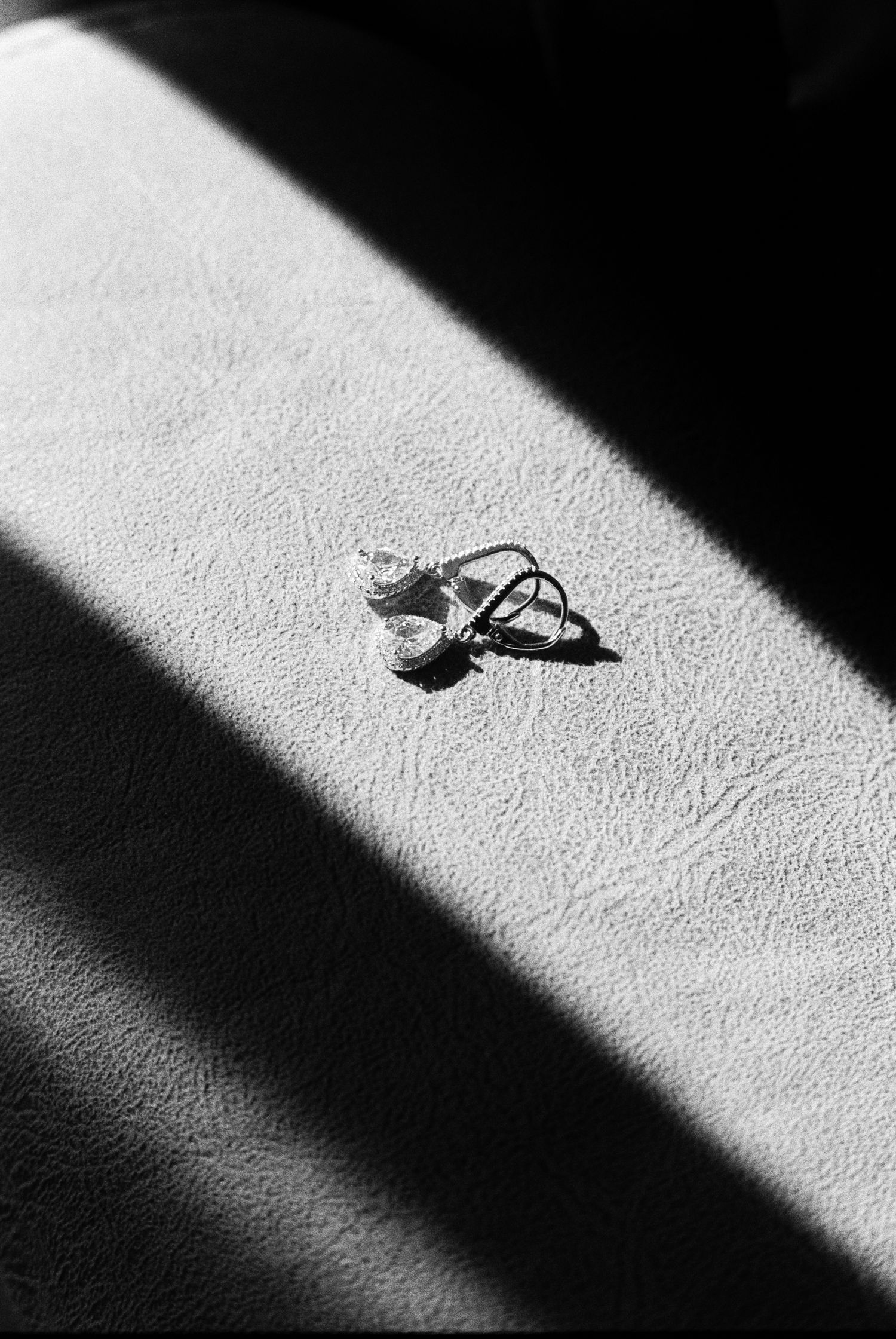 Black and white photo of diamond engagement ring casting shadow on textured white surface in sunlight.