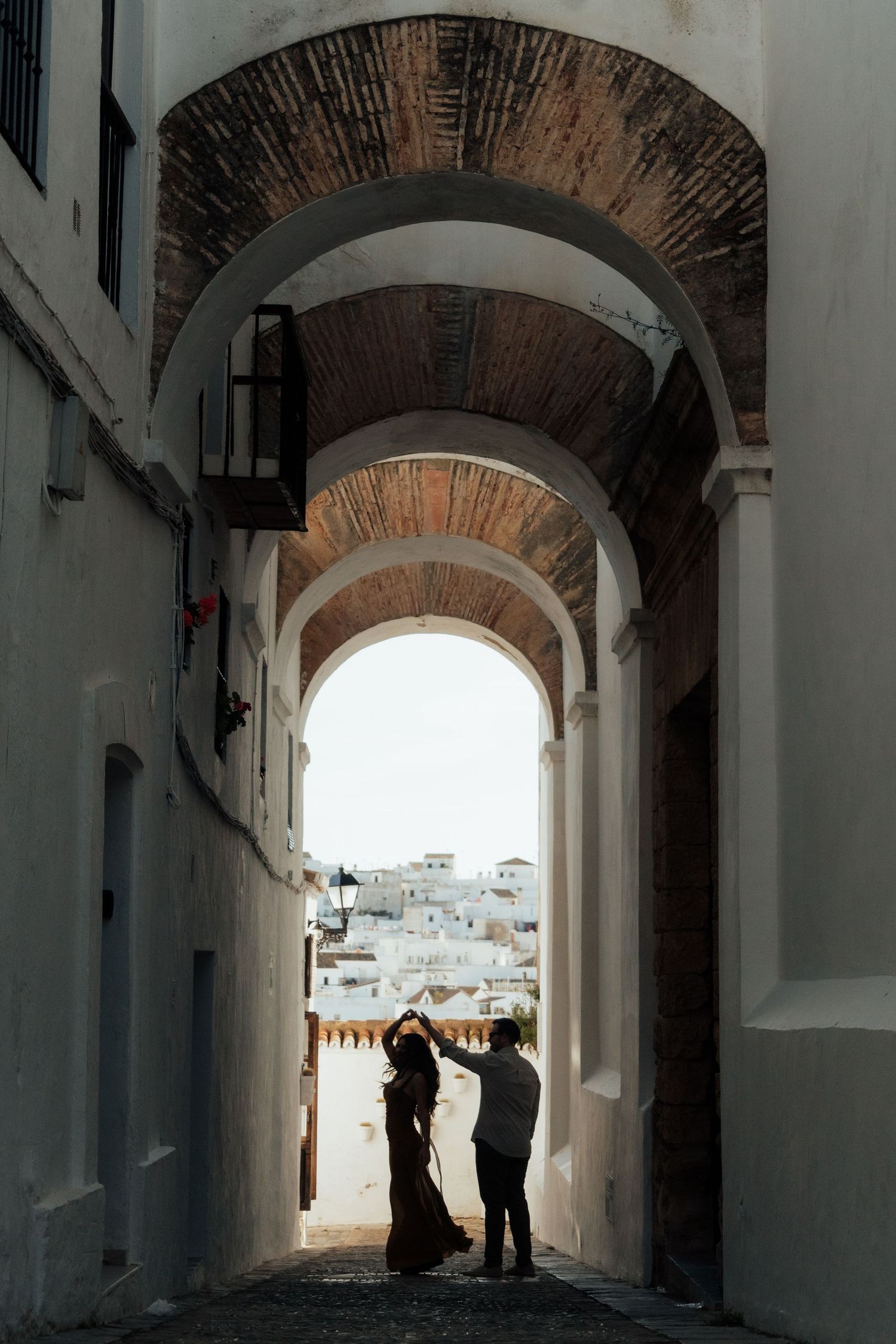 Couple dancing under a historic arched passageway in a white Mediterranean village.