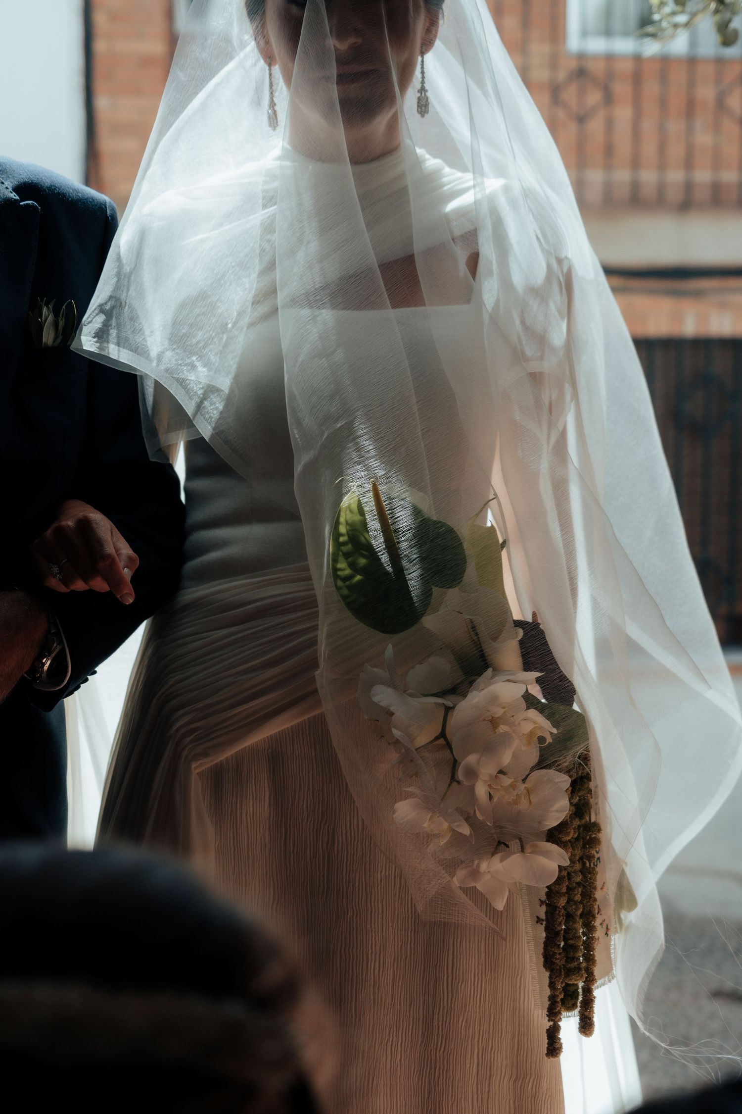 Close-up of bride in white veil holding elegant white floral bouquet with rosary beads.