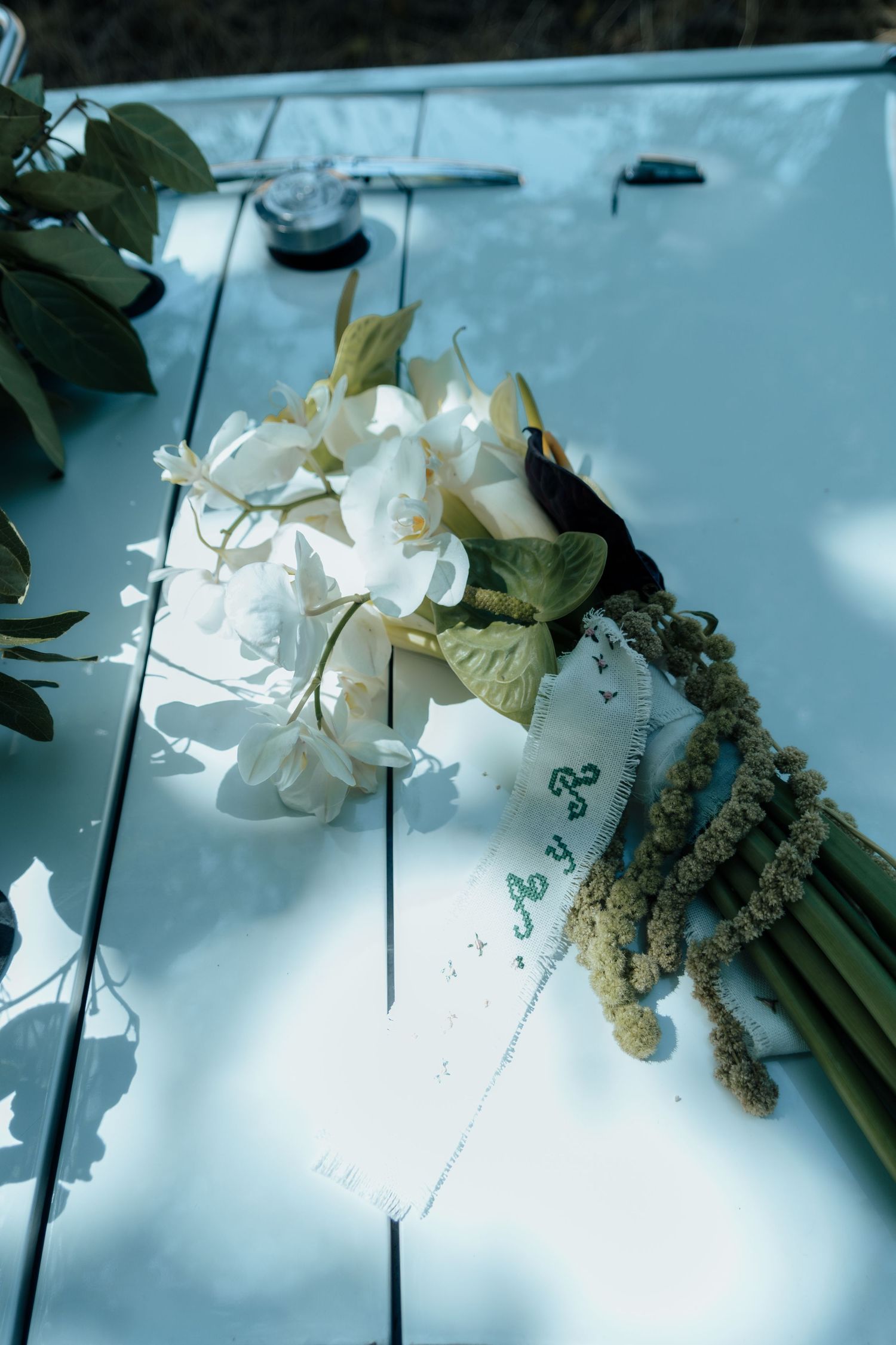 Elegant white orchid wedding bouquet with ribbon resting on the hood of a white vintage car.