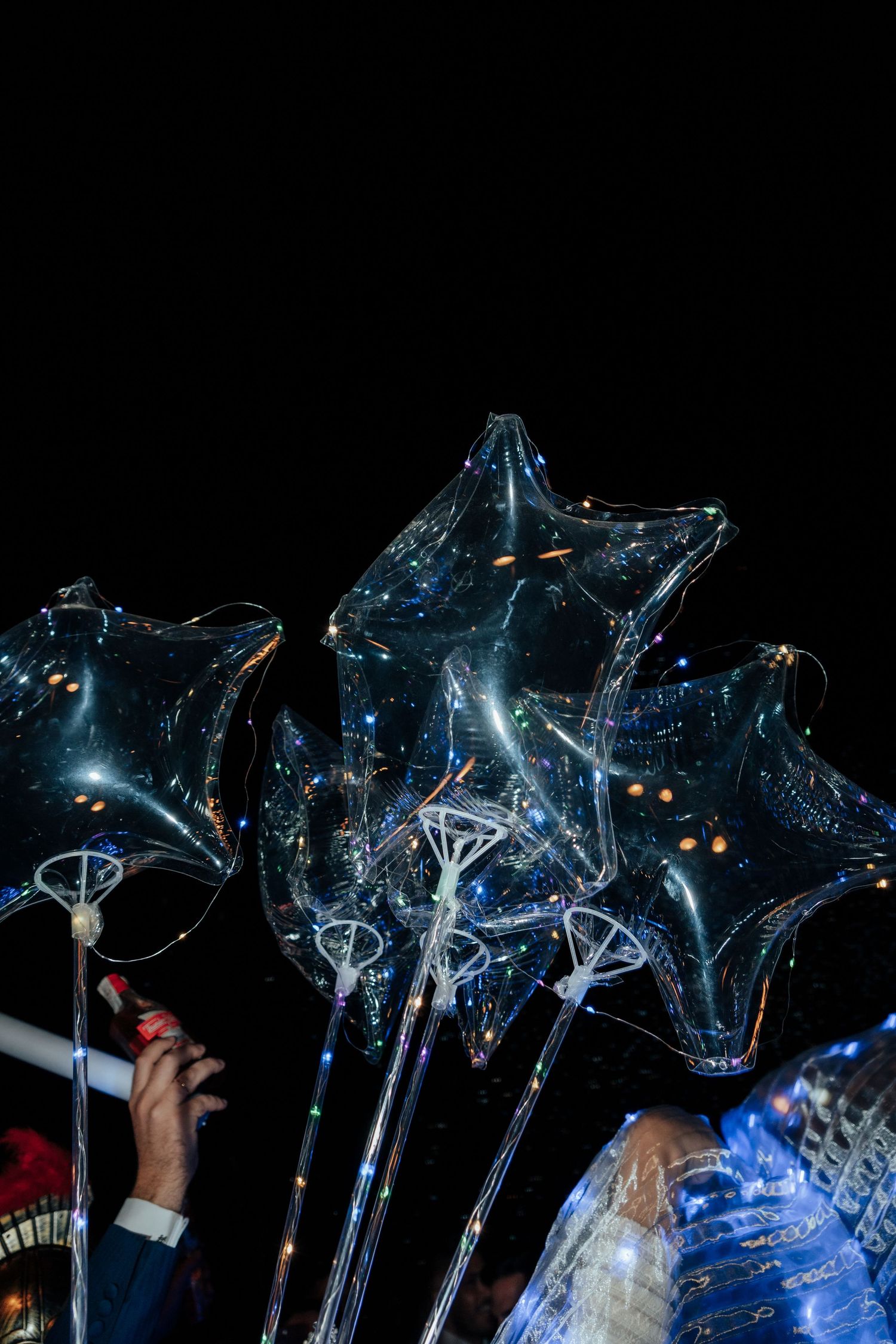 Transparent star-shaped balloons with LED lights glowing against a dark night sky at an outdoor celebration.