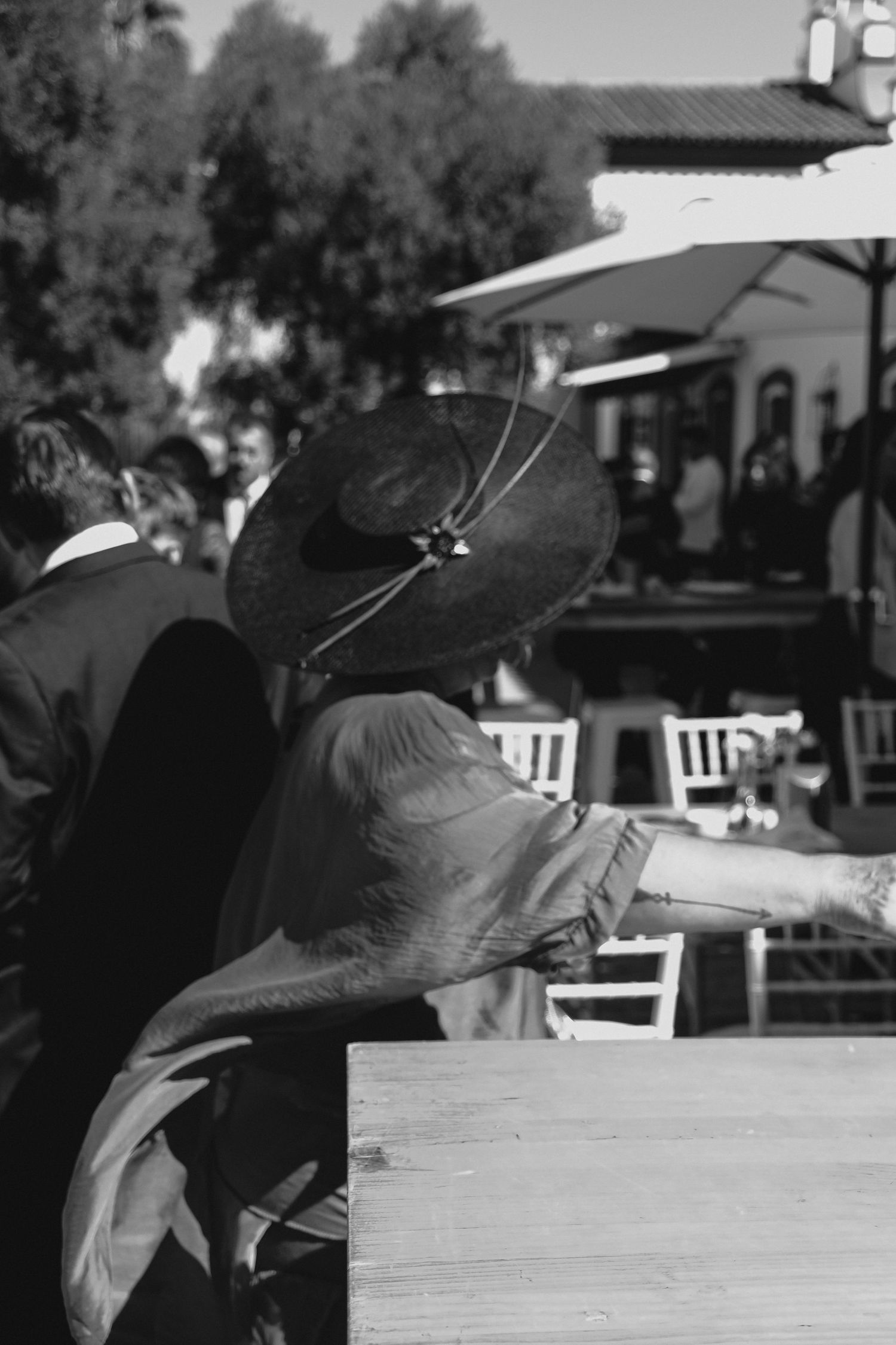 Elegant woman in wide-brim black hat at outdoor wedding reception in black and white photo.