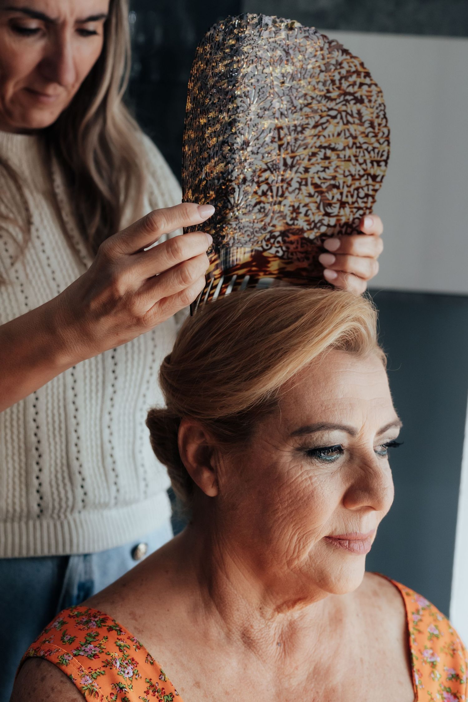 Hairstylist placing large decorative tortoiseshell comb into older blond womans updo hairstyle.