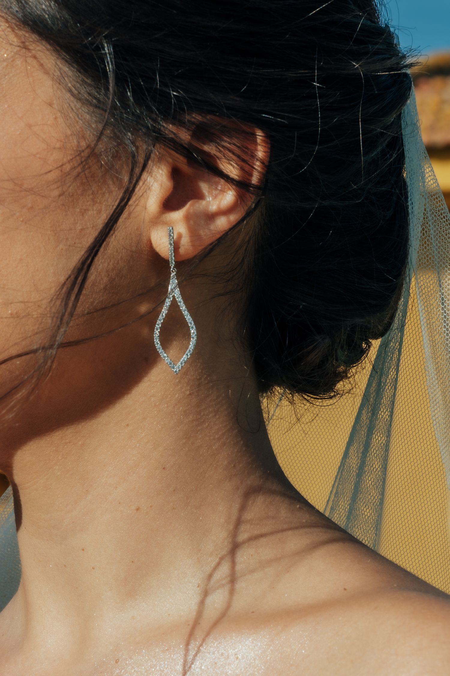 Close-up of a bride wearing elegant drop earrings with a sheer wedding veil behind her ear.