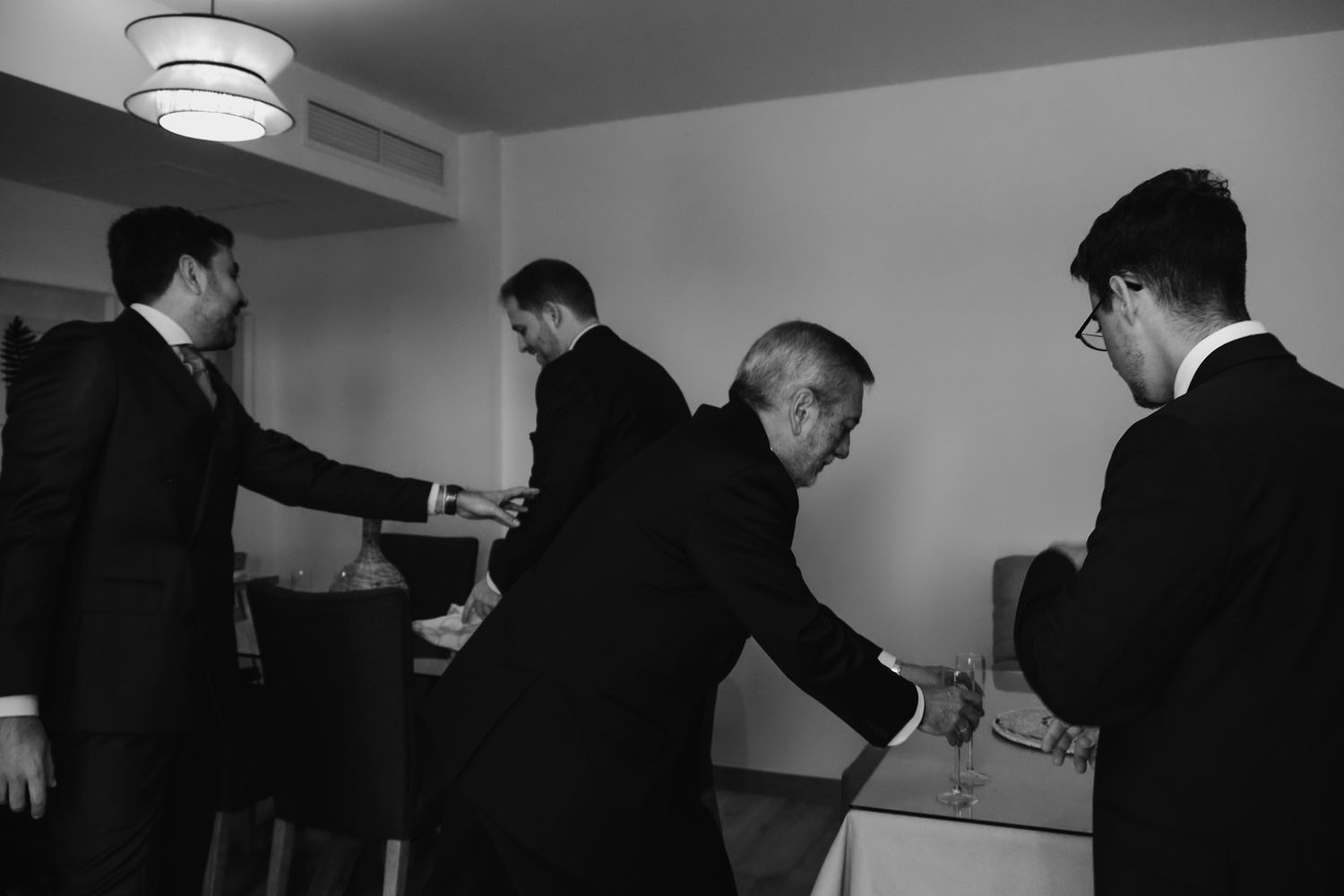 Black and white photo of groomsmen gathered around a table, sharing a celebratory moment before the wedding ceremony.
