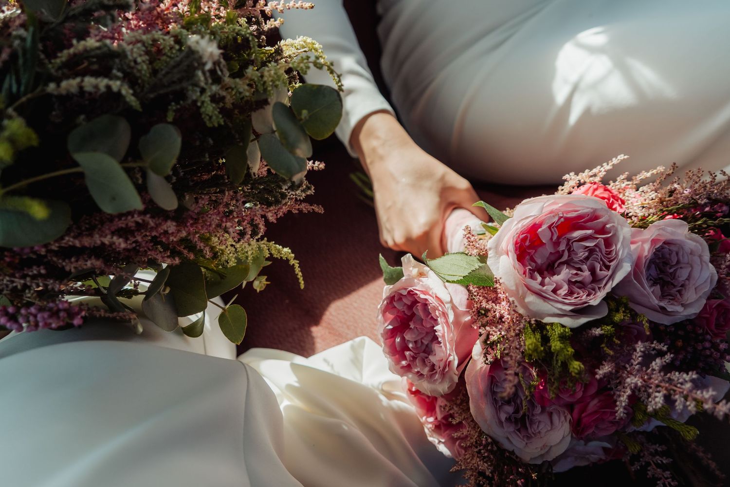 Bride holding a bouquet of pink and purple roses with eucalyptus in a white wedding gown.