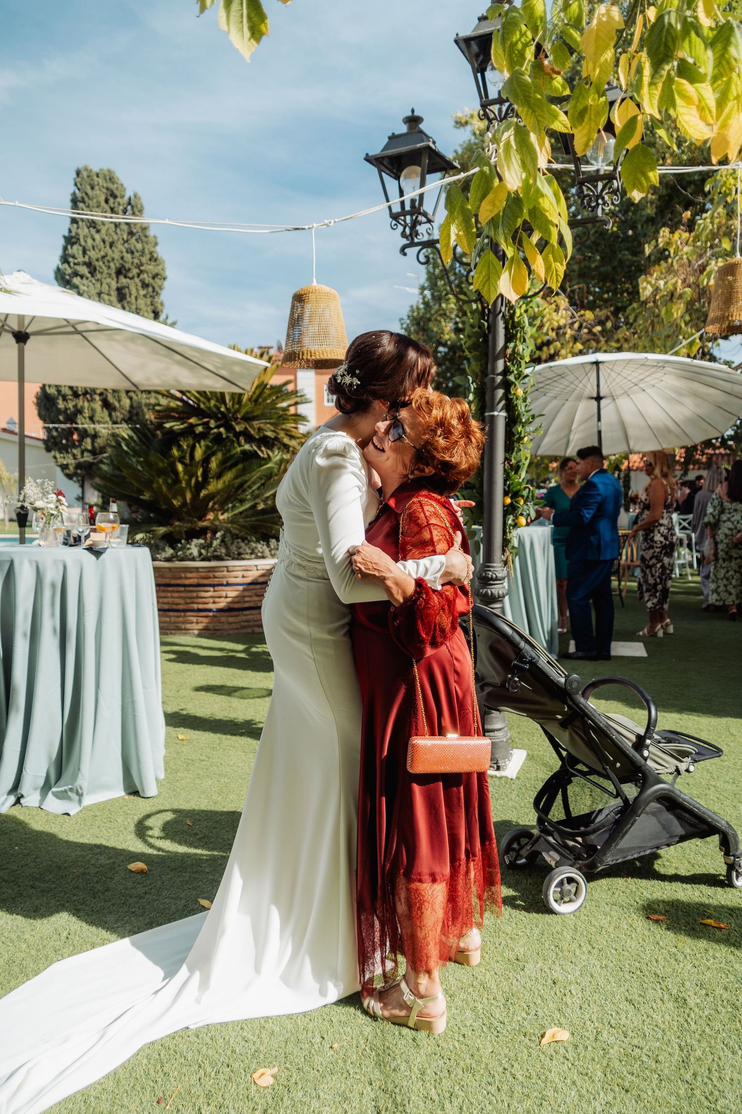 Bride in white gown embraces a guest in red dress at an outdoor garden wedding reception.
