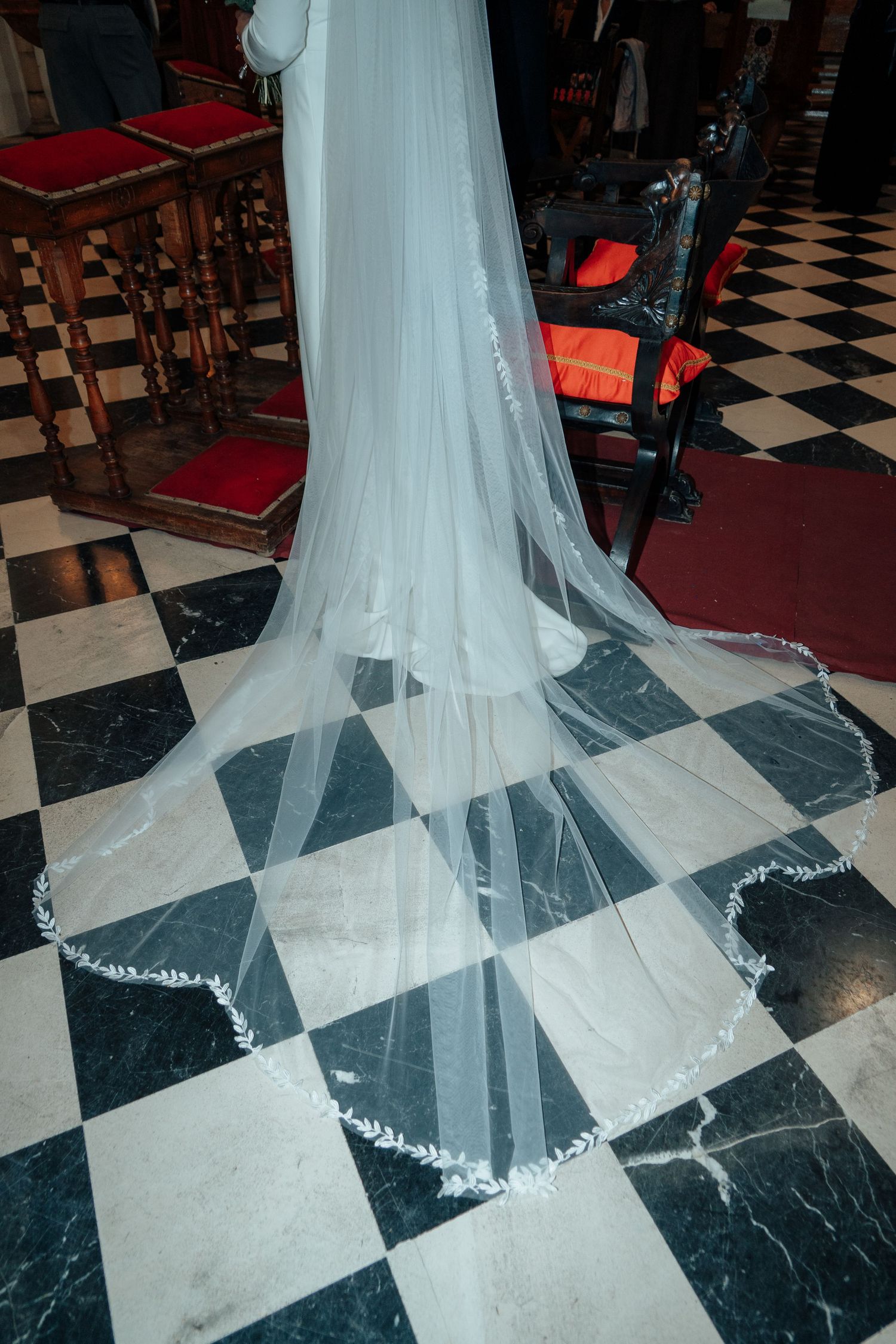 Elegant wedding veil with delicate floral embroidered trim spread across black and white marble floor.