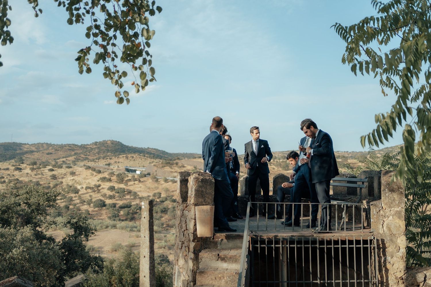 Groomsmen in suits gathered on stone terrace overlooking arid landscape at wedding venue.