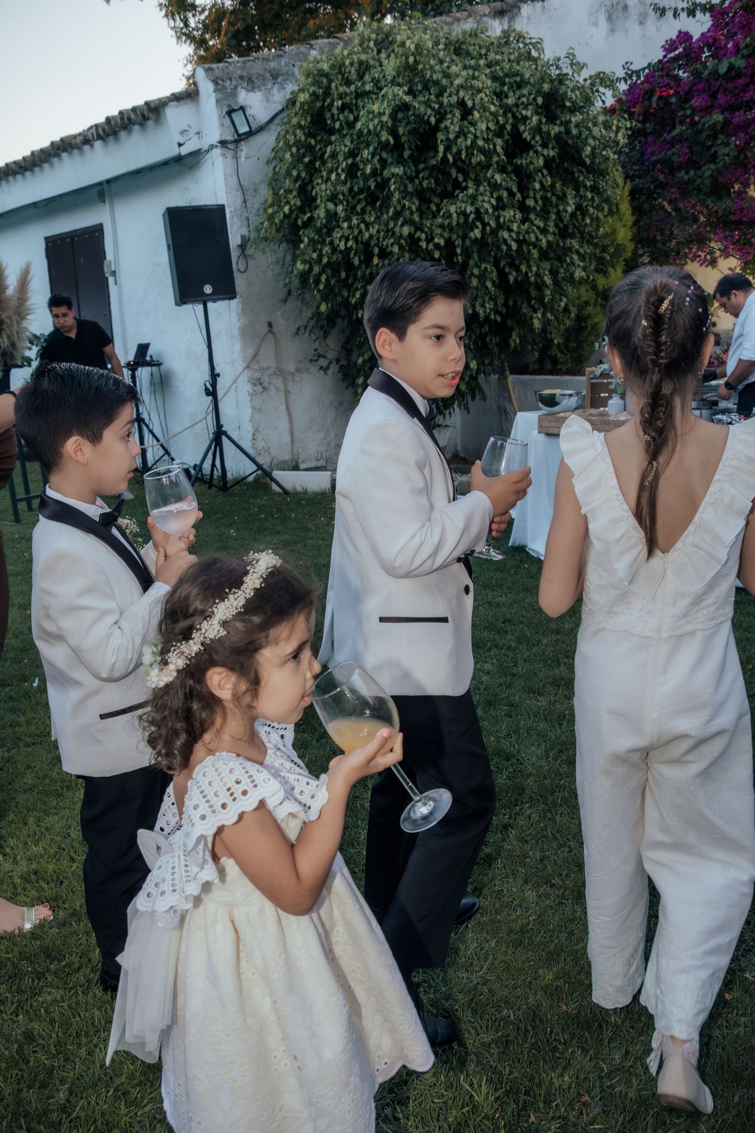 Children dressed in formal wedding attire enjoying outdoor reception celebration.