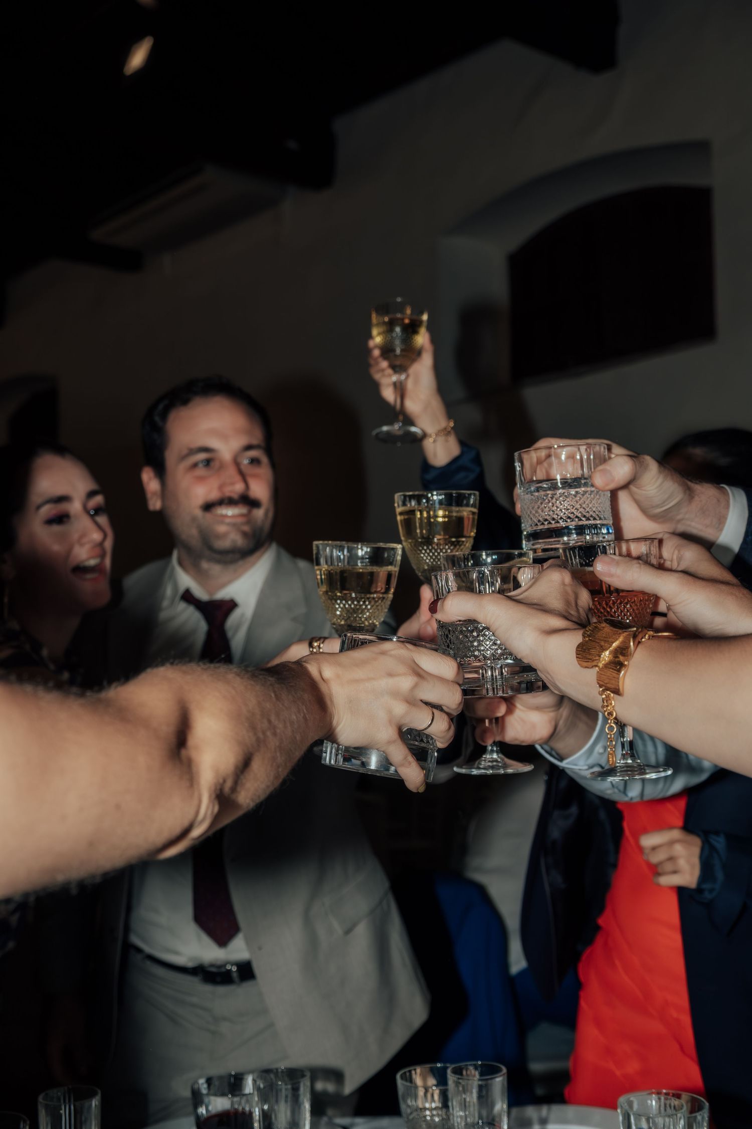 Group of wedding guests raising crystal glasses in a joyful toast at indoor reception celebration.