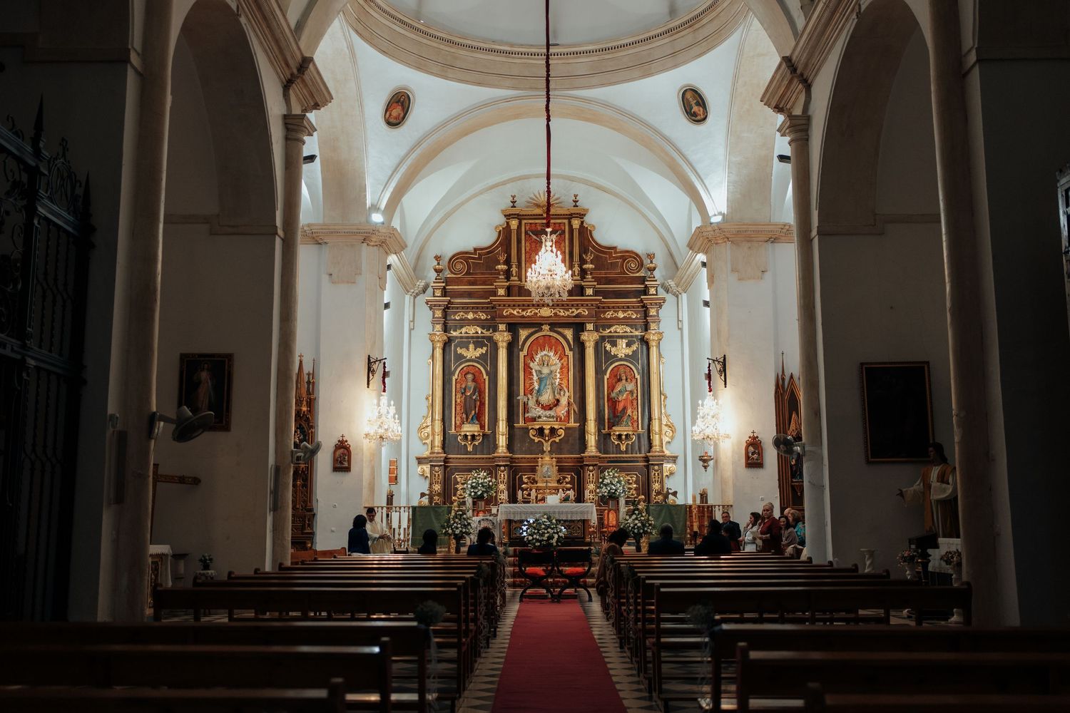 Ornate Catholic church interior with golden altar, wooden pews, and arched ceiling during a wedding ceremony.