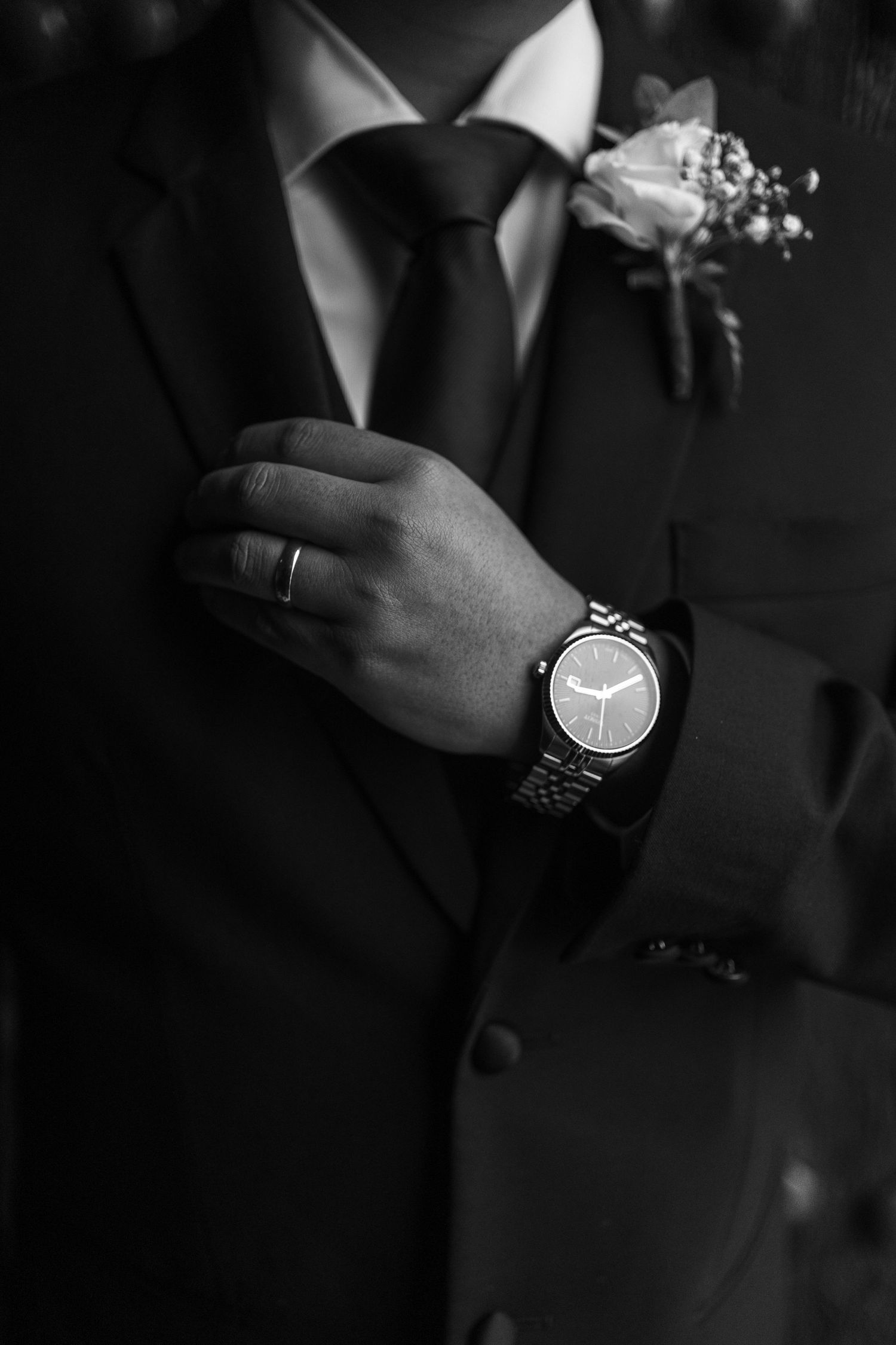 Black and white close-up of a groom adjusting his suit jacket, showcasing his watch and wedding ring.
