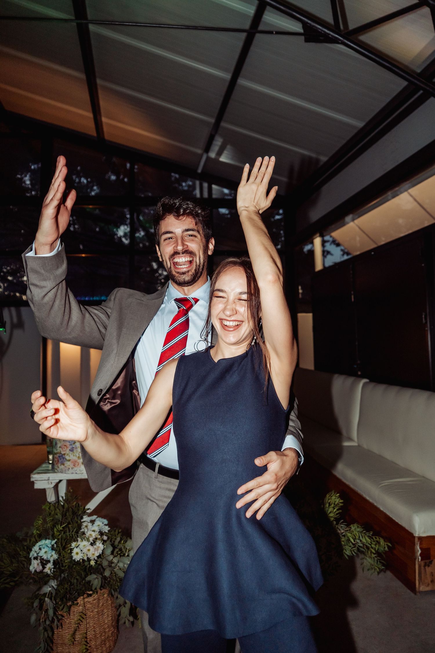 Happy couple celebrating at a wedding reception, both raising hands and smiling under venue lights.