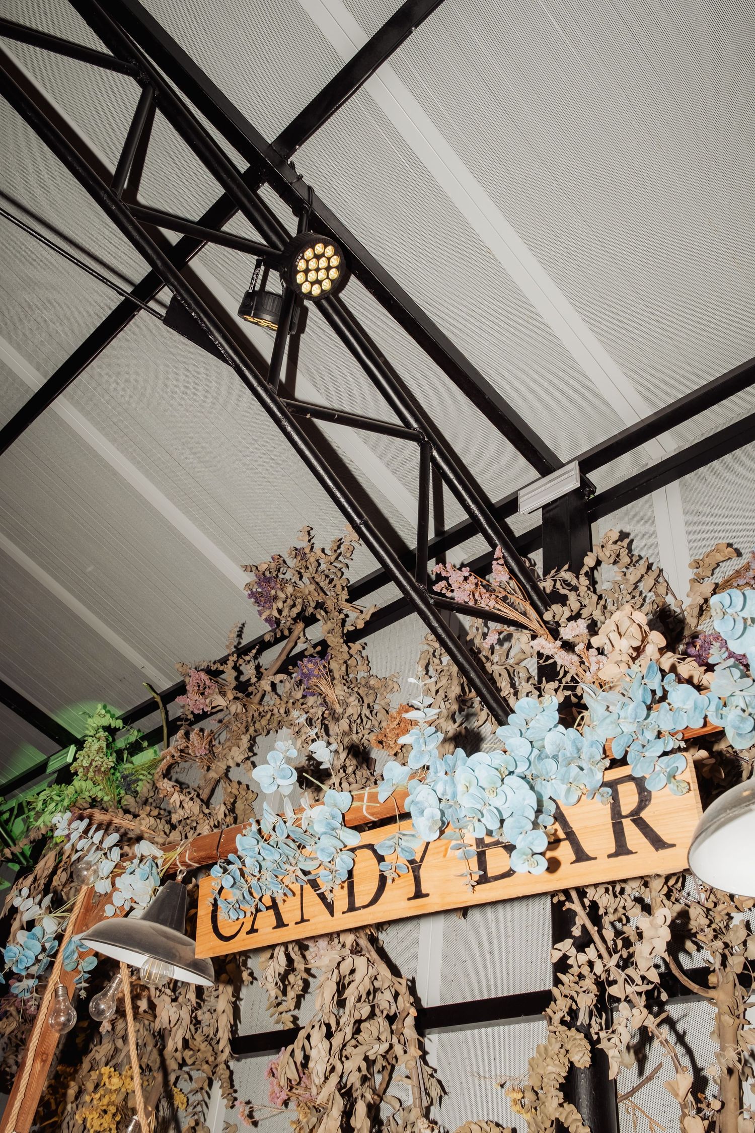 Rustic Candy Bar sign surrounded by dried floral decorations under industrial ceiling beams.