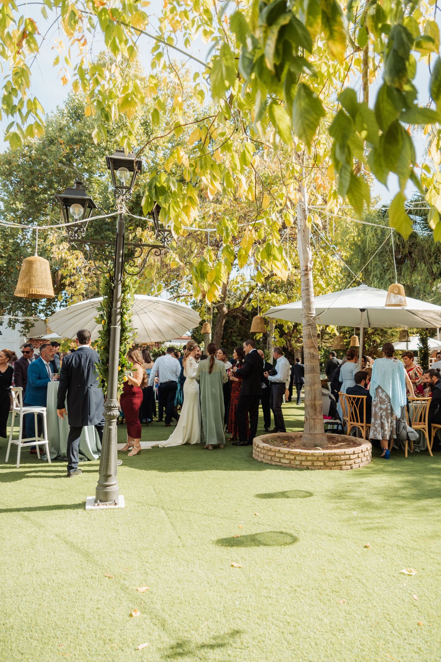 Wedding guests mingling under umbrellas in a sunlit garden reception.