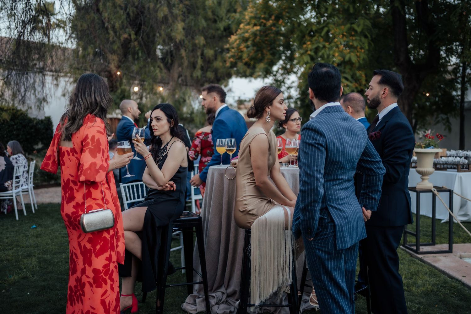 Wedding guests socializing at outdoor evening cocktail reception in garden venue.