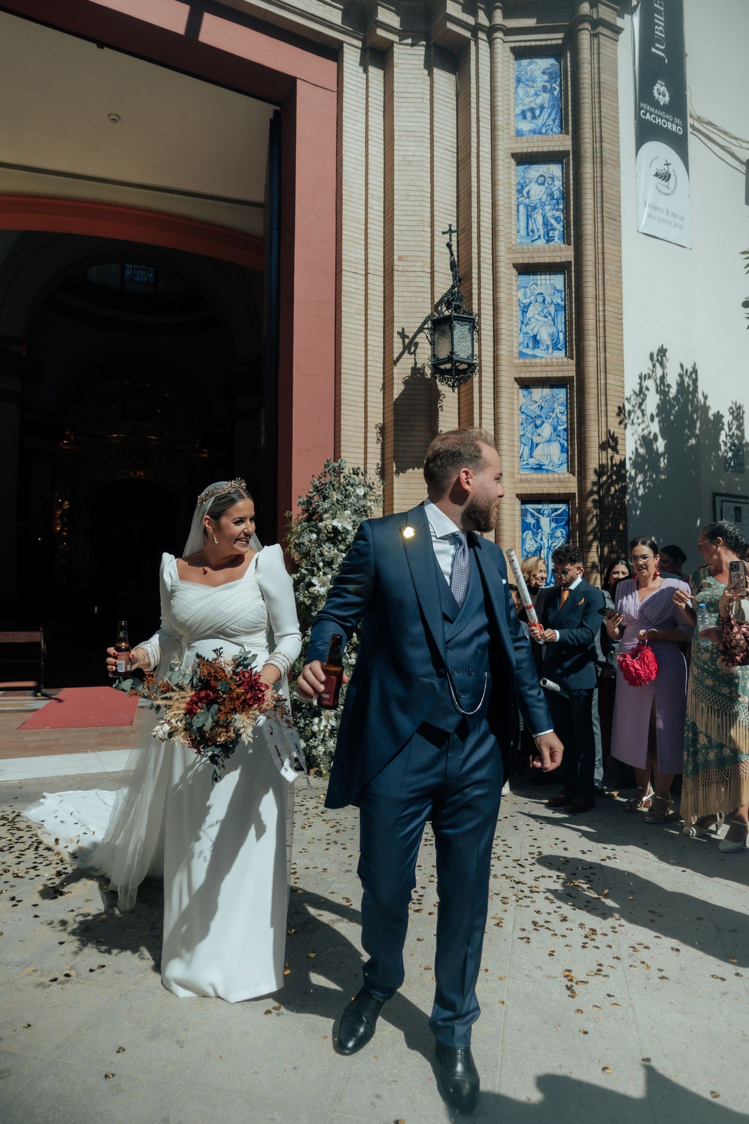 Bride holding colorful bouquet and groom in navy suit walk hand in hand from church.