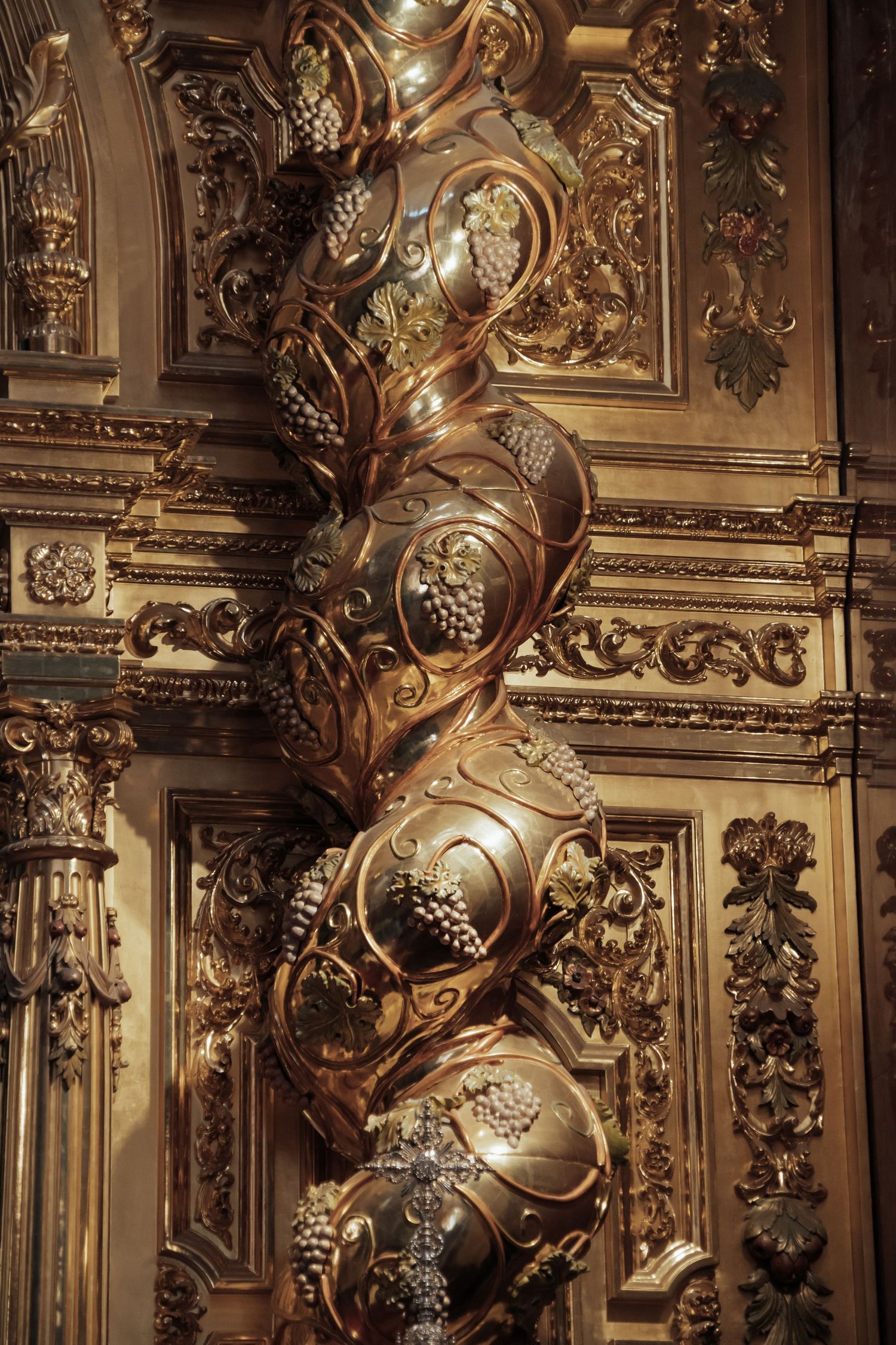 Ornate gilded Solomonic column with grape motifs in elaborate baroque church interior.