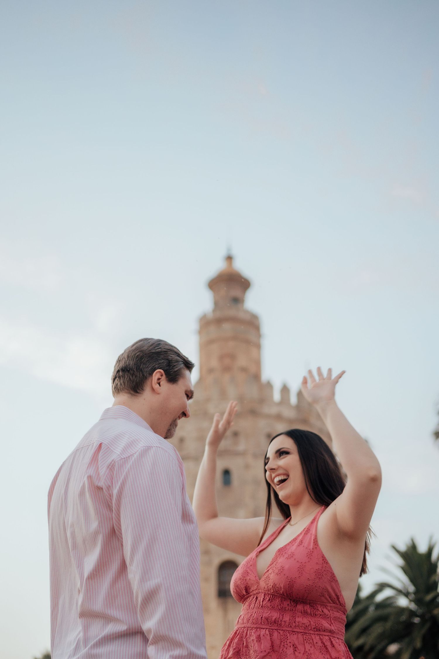 Joyful couple laughing together with Torre del Oro tower in Seville sky background.