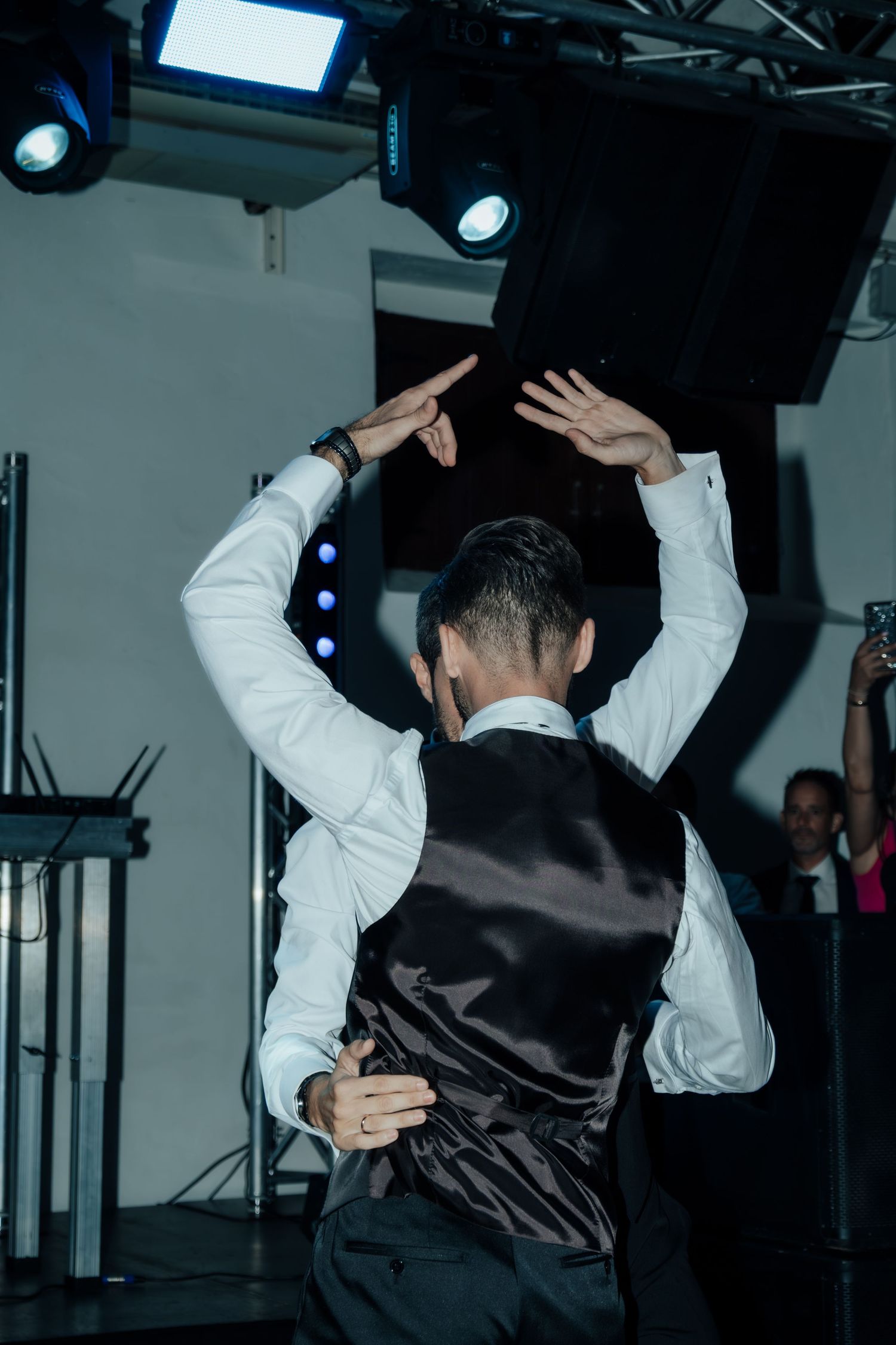 Man in white shirt and dark vest dancing with arms raised at wedding reception party.
