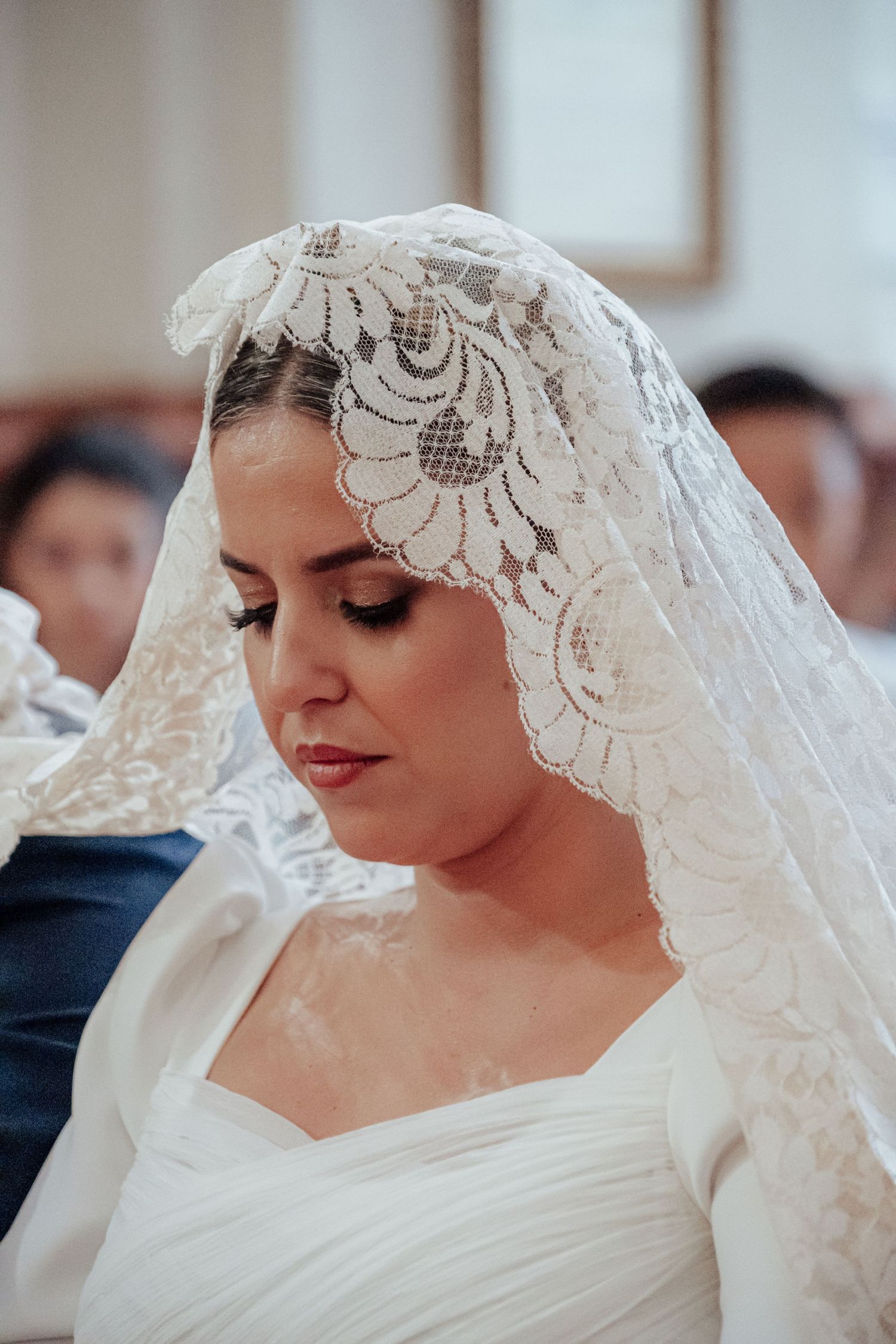 Beautiful bride wearing intricate lace mantilla veil during traditional church wedding ceremony.
