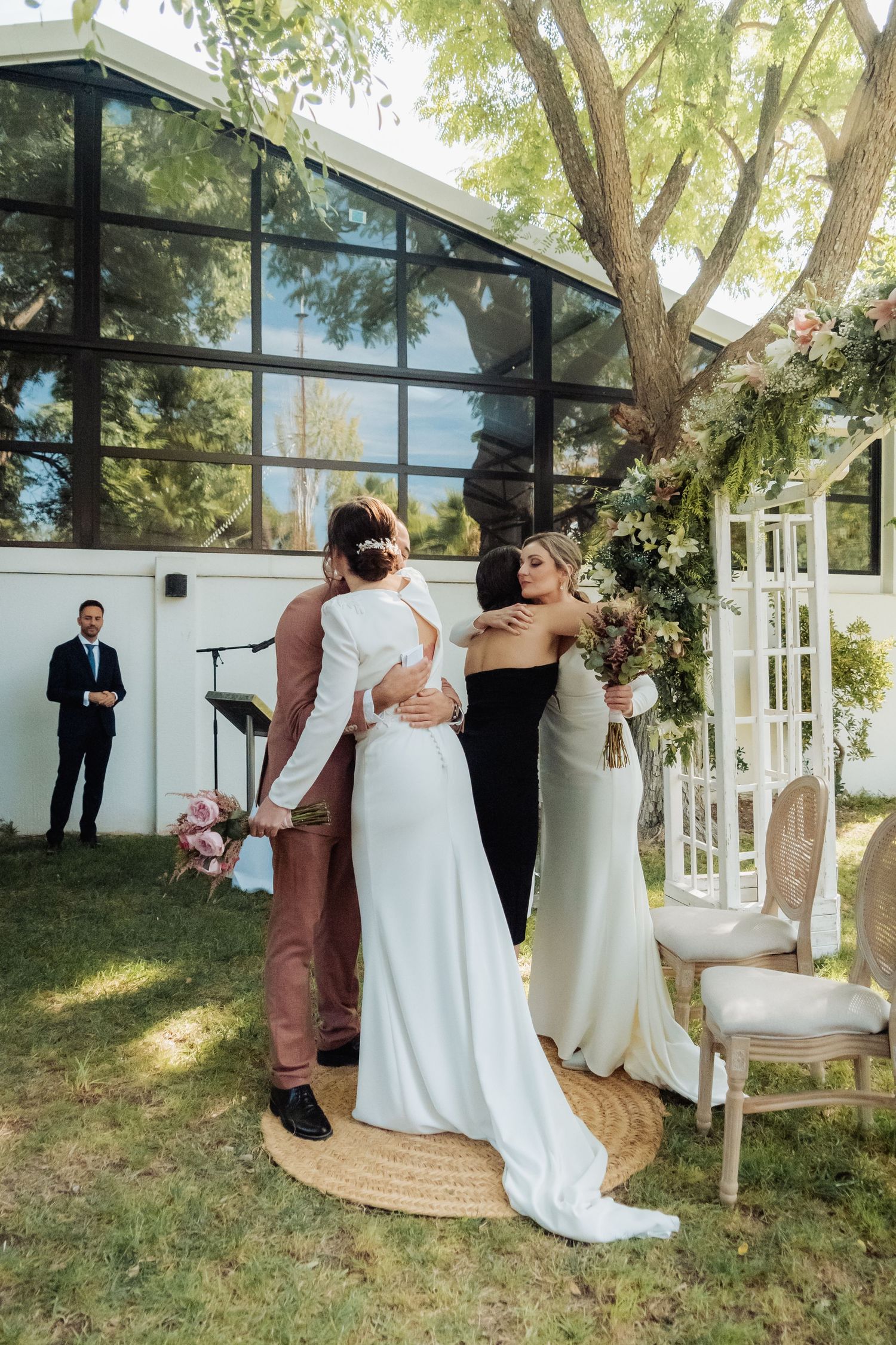 Two brides embracing their officiant after their outdoor garden wedding ceremony concludes.