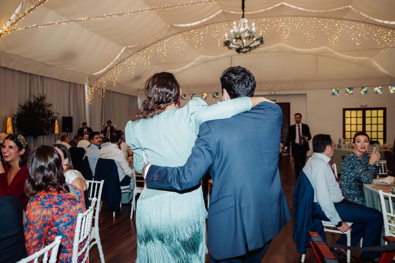 Couple embracing on wedding reception dance floor under fairy light draped marquee ceiling.